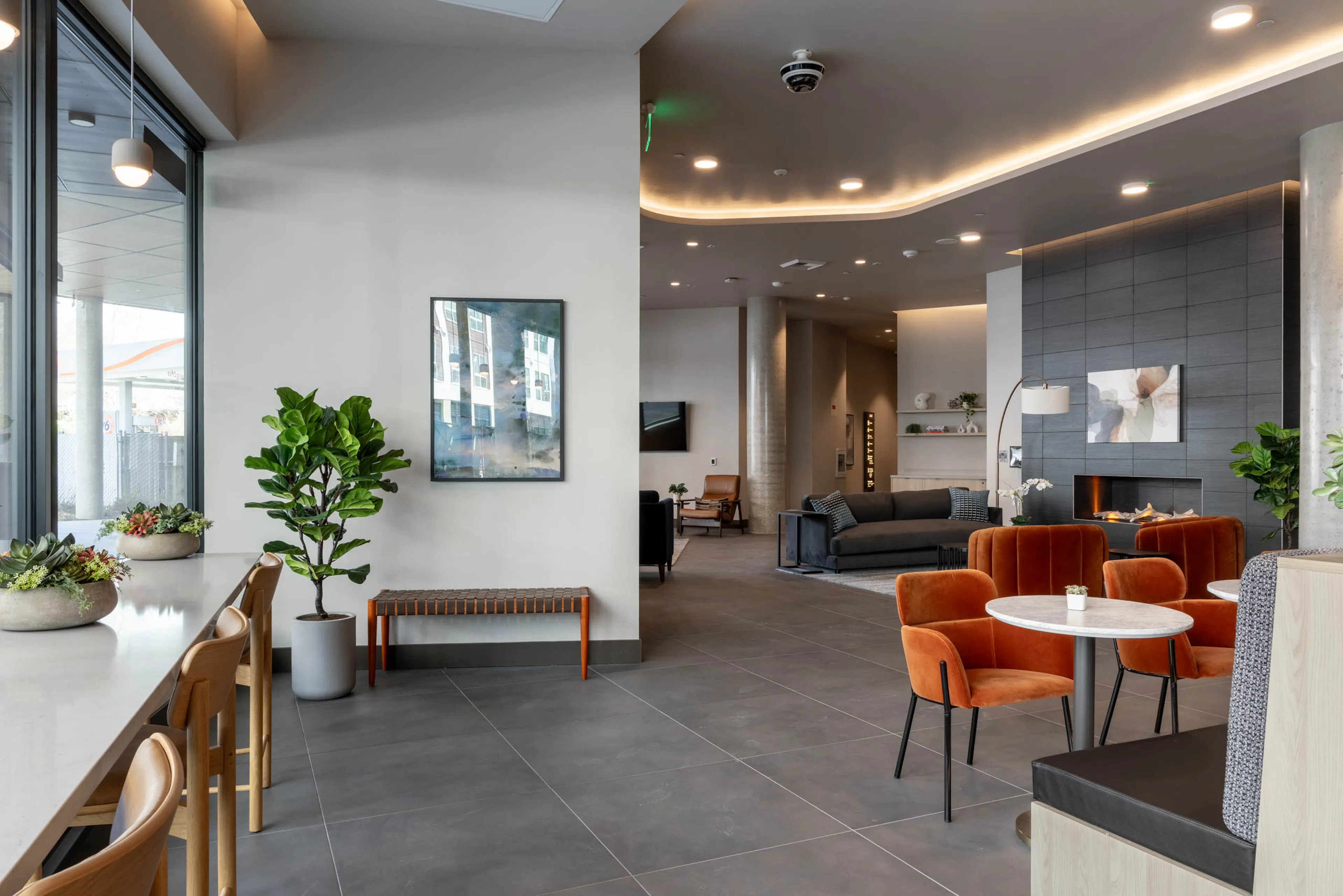 Community clubroom with multiple social and work-from-home spaces, featuring a large gray fireplace and gray furniture nearby.