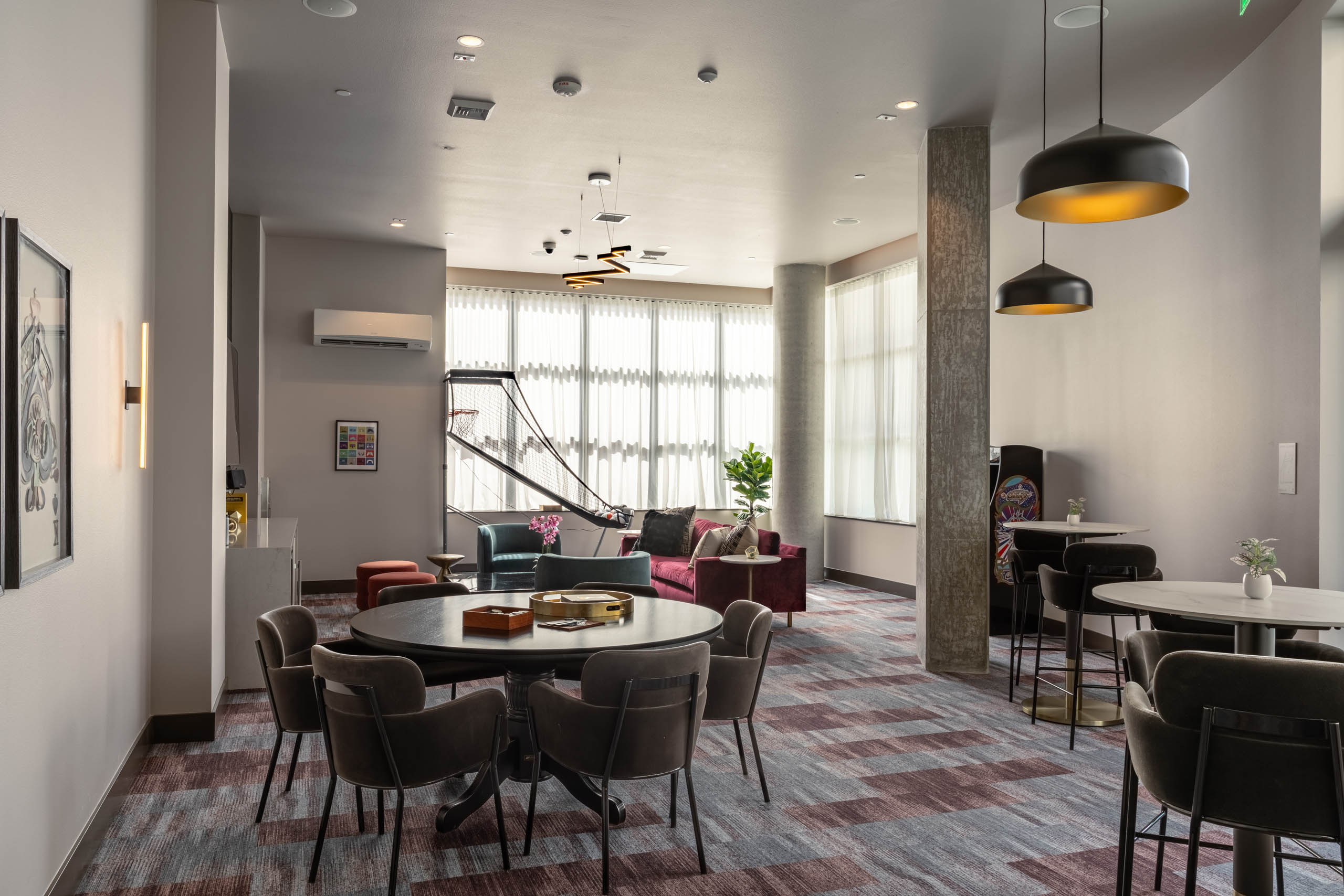 Clubroom area with varied seating and a basketball arcade game machine in the background, offering multiple spaces for socializing.