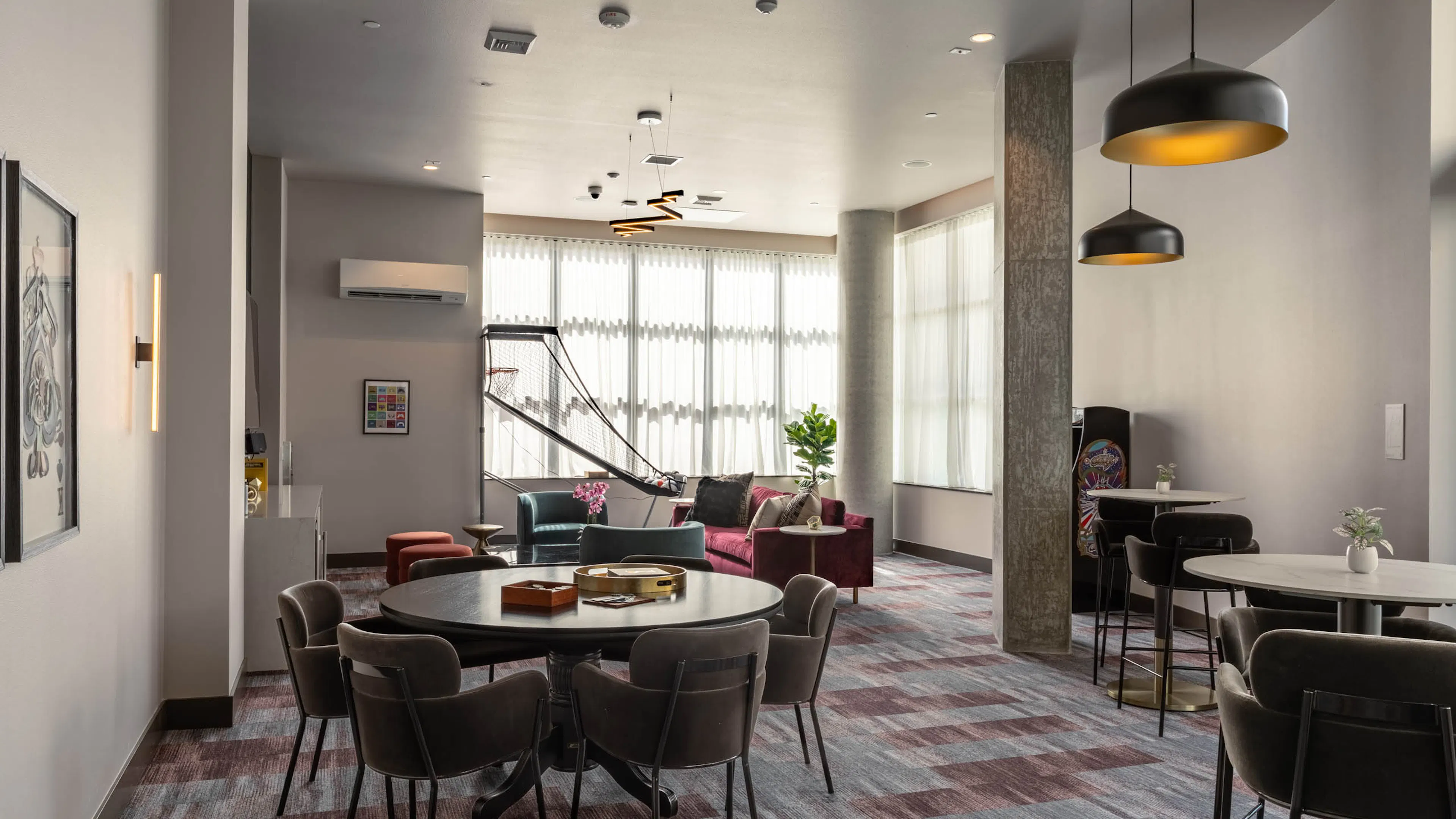 Clubroom area with varied seating and a basketball arcade game machine in the background, offering multiple spaces for socializing.