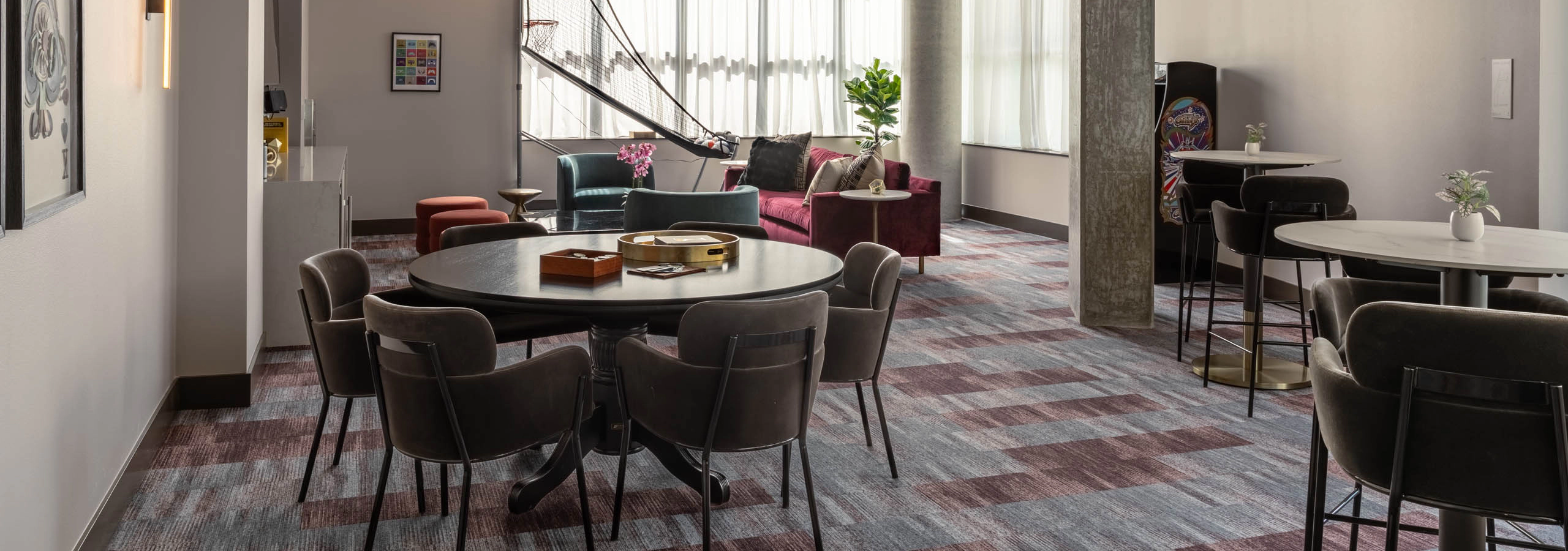 Clubroom area with varied seating and a basketball arcade game machine in the background, offering multiple spaces for socializing.
