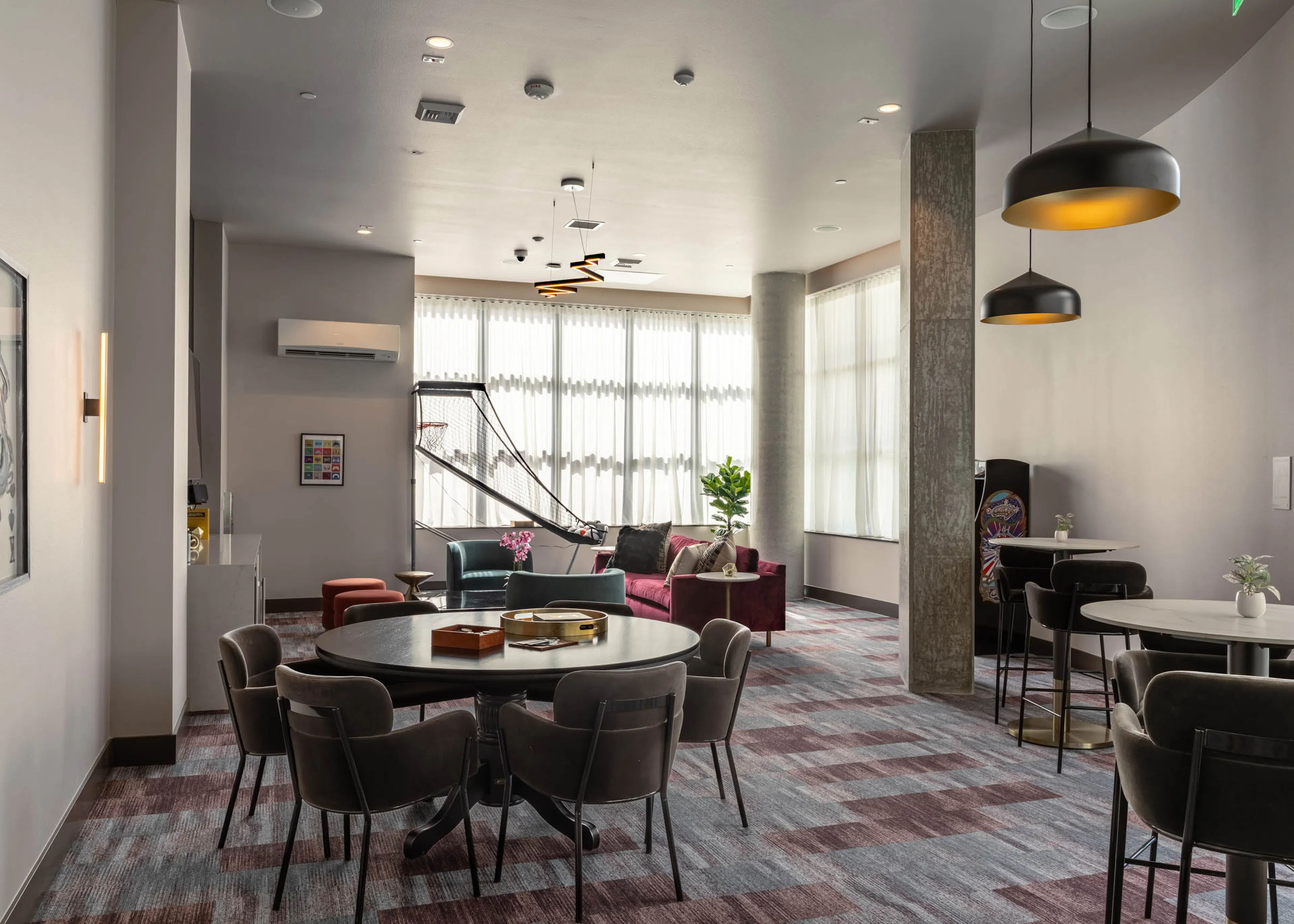 Clubroom area with varied seating and a basketball arcade game machine in the background, offering multiple spaces for socializing.