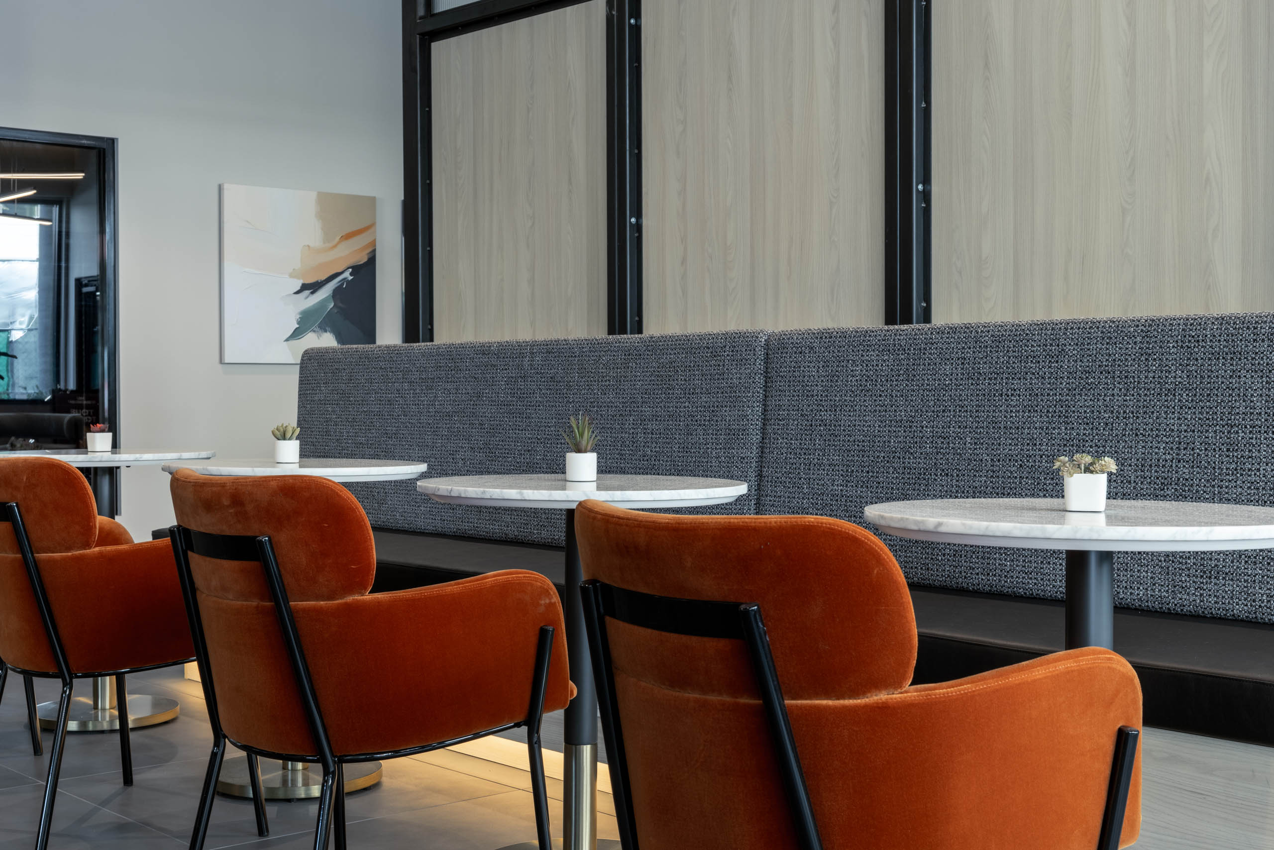 Social and co-working space with three round white tables, orange chairs, and long built-in bench seating opposite.