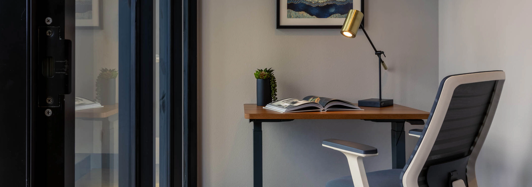 Work-from-home space with a wooden desk and chair, floor-to-ceiling windows, white walls, and blue carpet.