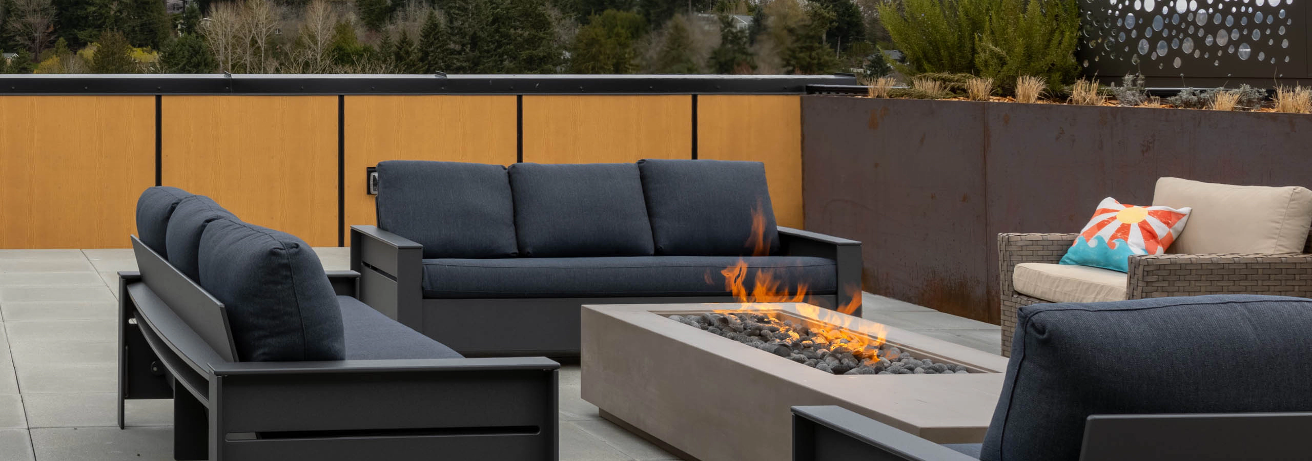 Gray three-piece chairs and a single chair surround an open firepit on a rooftop terrace.