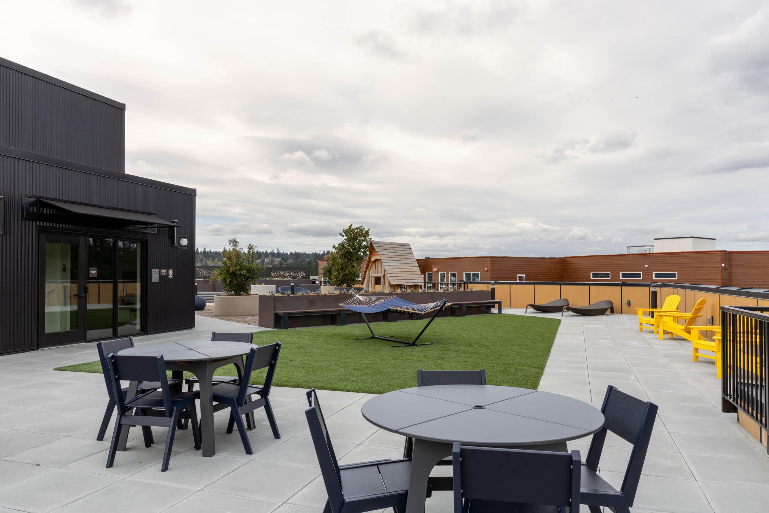 Rooftop terrace with turf patch in the middle, two gray tables with four chairs, blue hammocks, and yellow deck chairs.
