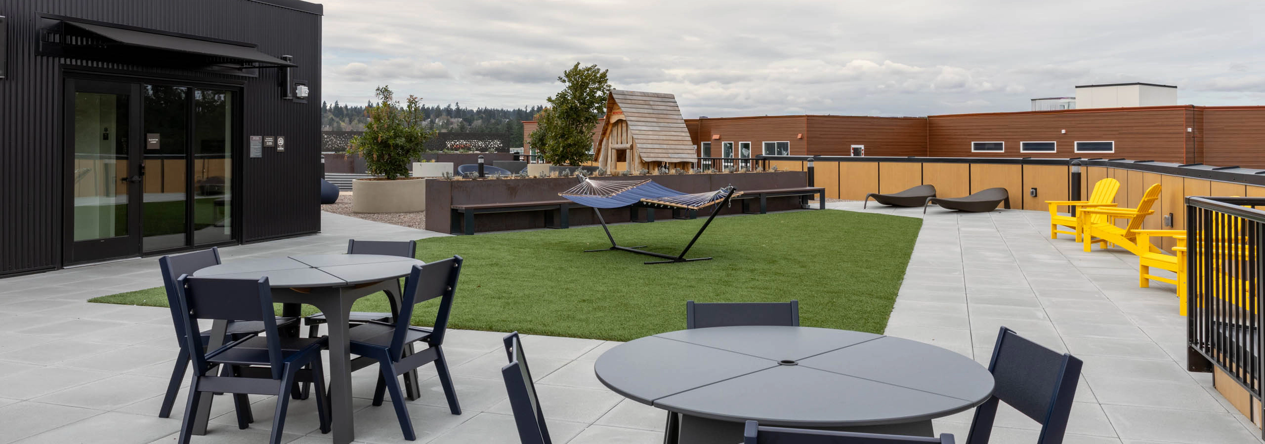 Rooftop terrace with turf patch in the middle, two gray tables with four chairs, blue hammocks, and yellow deck chairs.