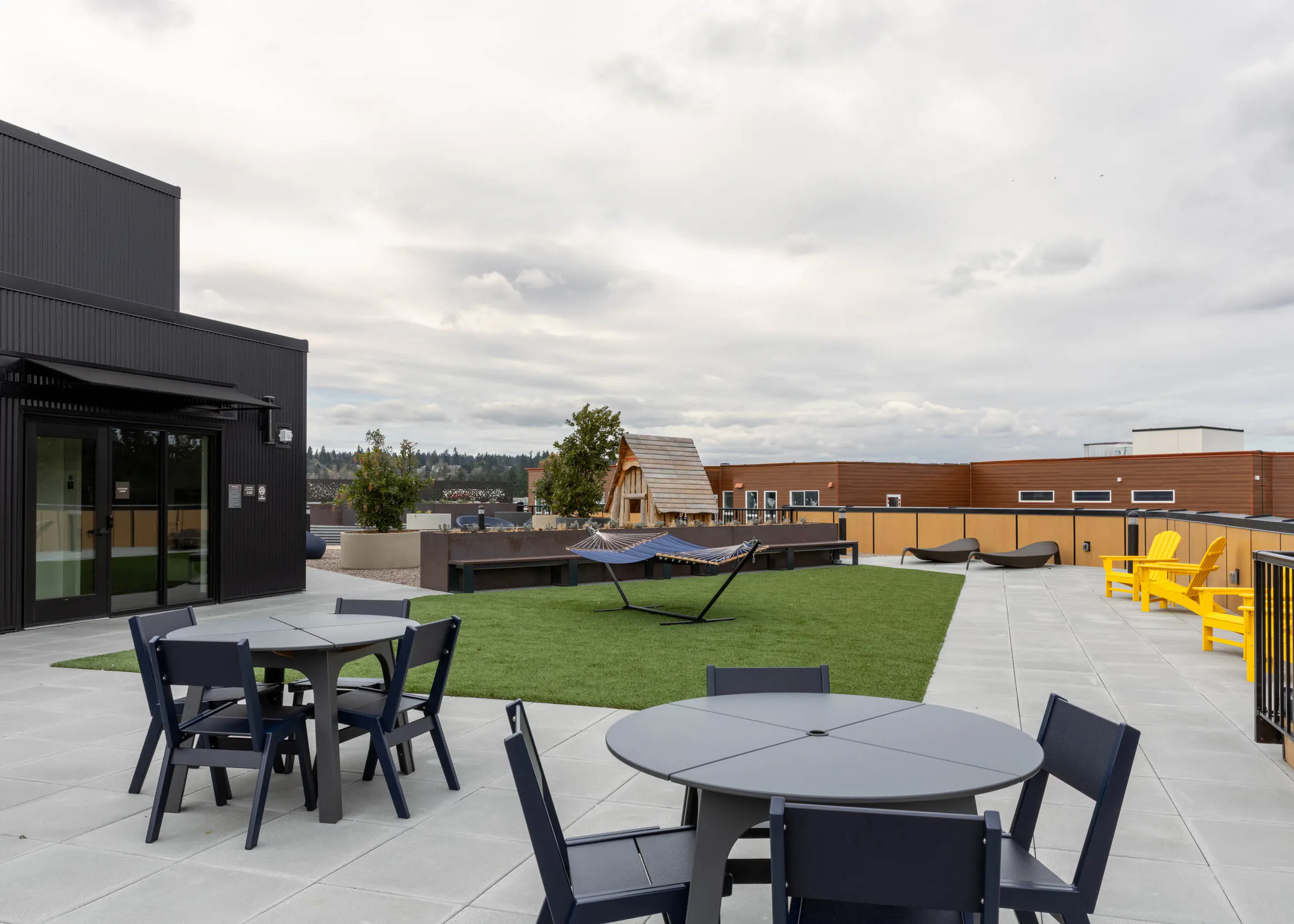 Rooftop terrace with turf patch in the middle, two gray tables with four chairs, blue hammocks, and yellow deck chairs.