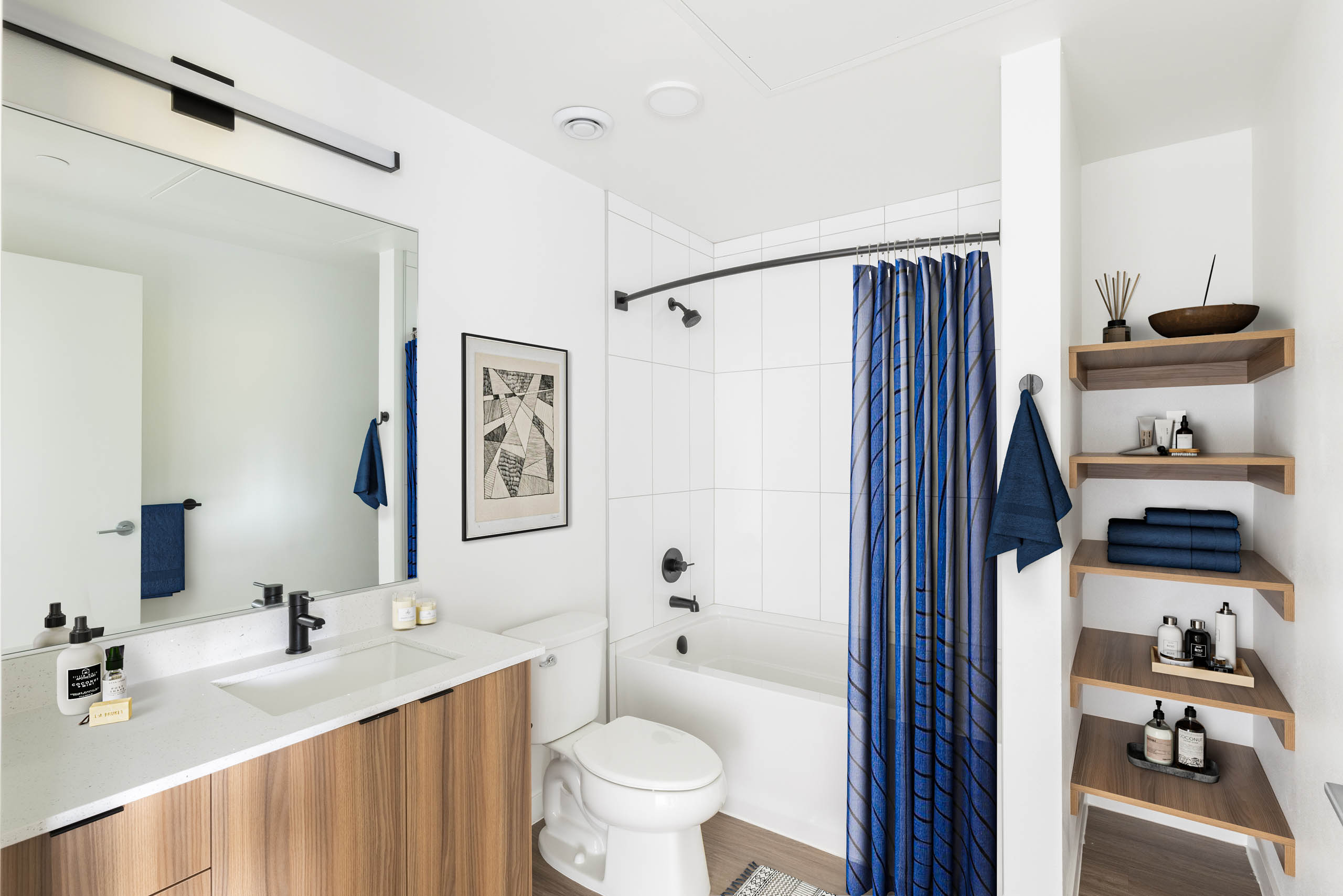 Interior view of AMLI Redmond Way apartment bathroom with soaking tub, open wood shelving, and large mirror with modern vanity.