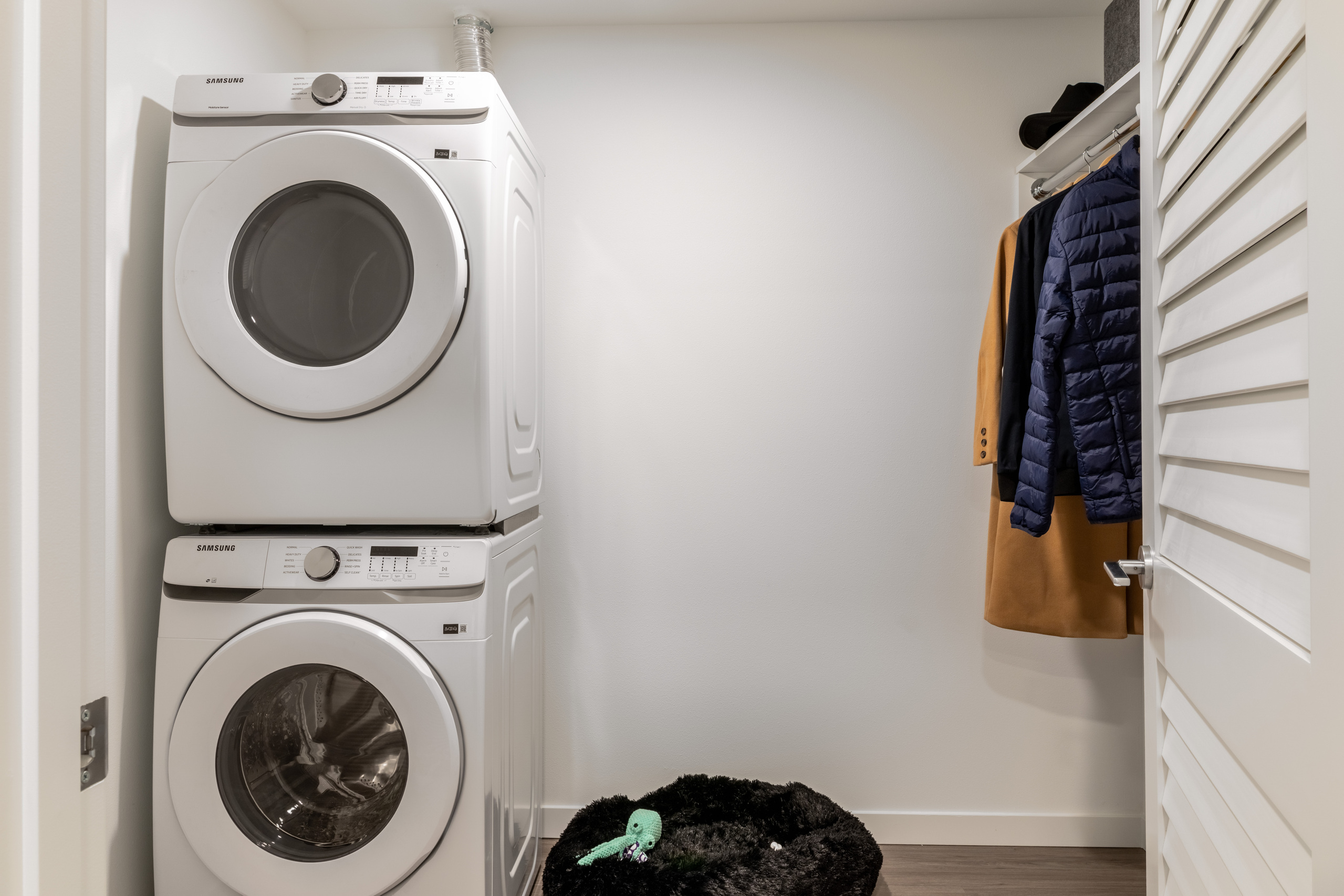 Closet area with white walls, with in-unit washer and dryer appliances, next to large storage space with space to hang clothes.