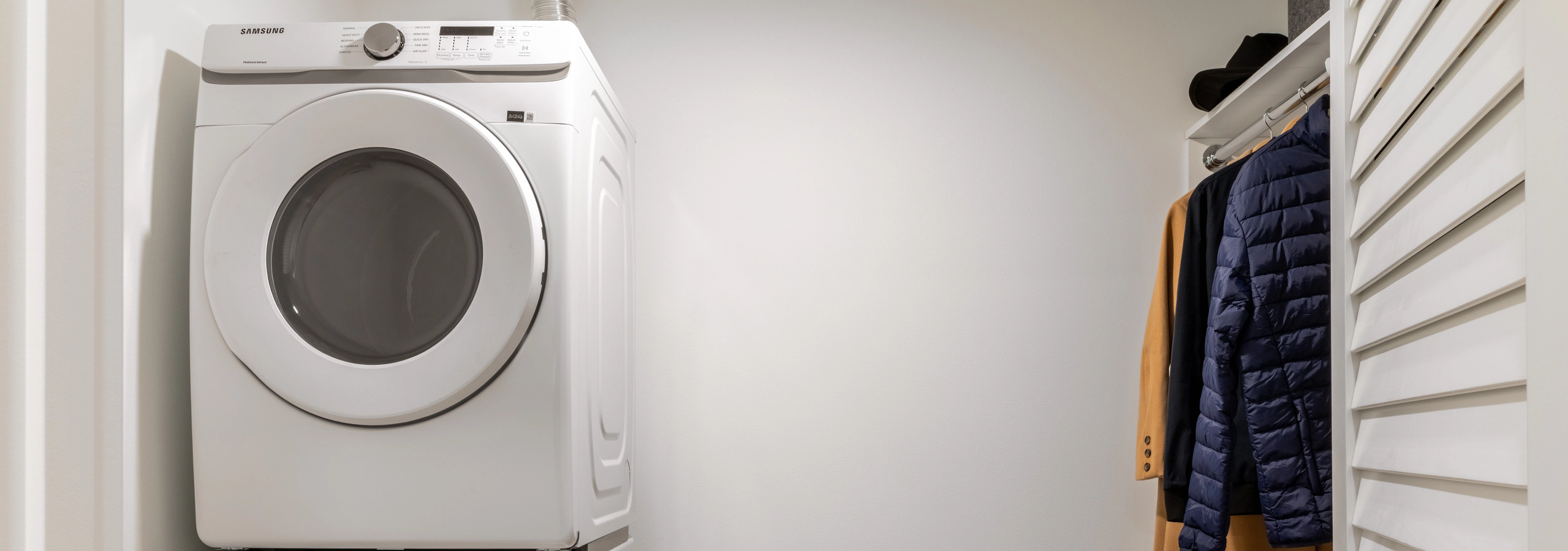 Closet area with white walls, with in-unit washer and dryer appliances, next to large storage space with space to hang clothes.