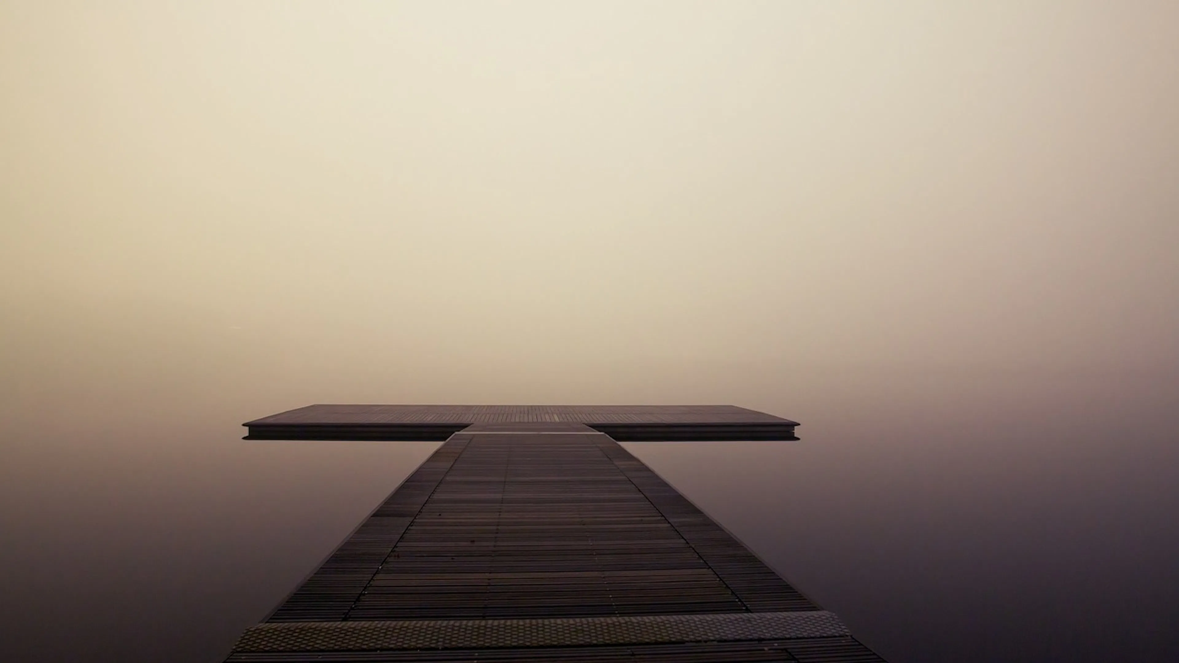 A small t shaped pier stretching over a still calm lake in heavy fog