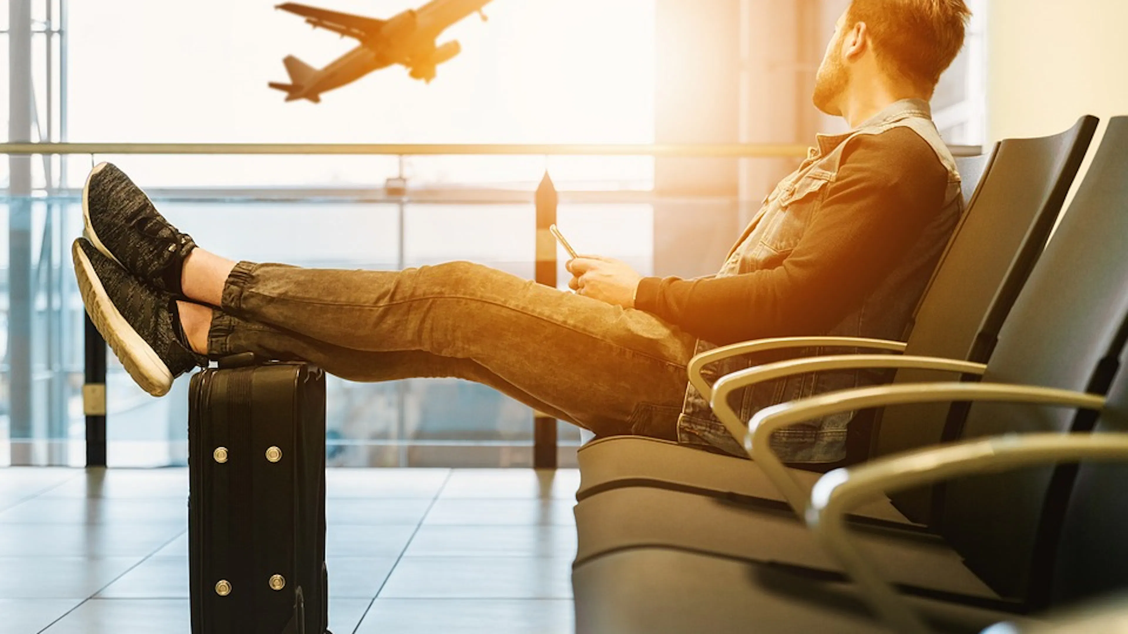 A person resting his feet on a small suitcase in an airport waiting chair