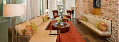 Interior of AMLI RidgeGate clubroom with sheer curtains, gold tone suede sectional facing stacked tone wall and flat panel TV