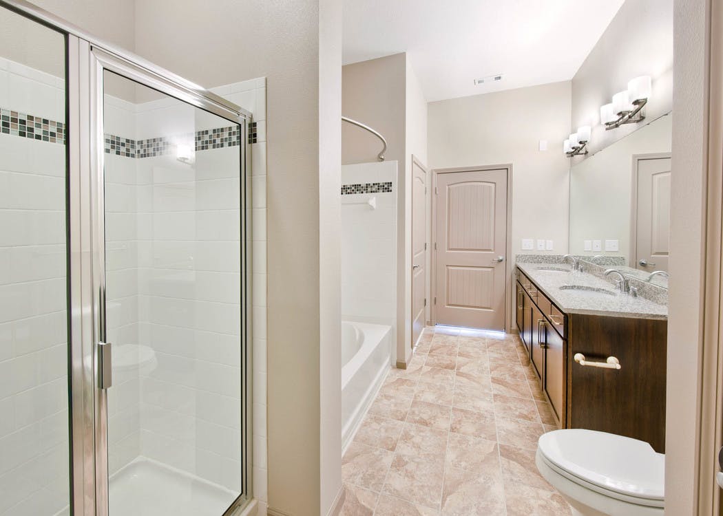 Bathroom at AMLI North Point with a double vanity sink and a white tiled bathtub next to a shower with frosted glass doors