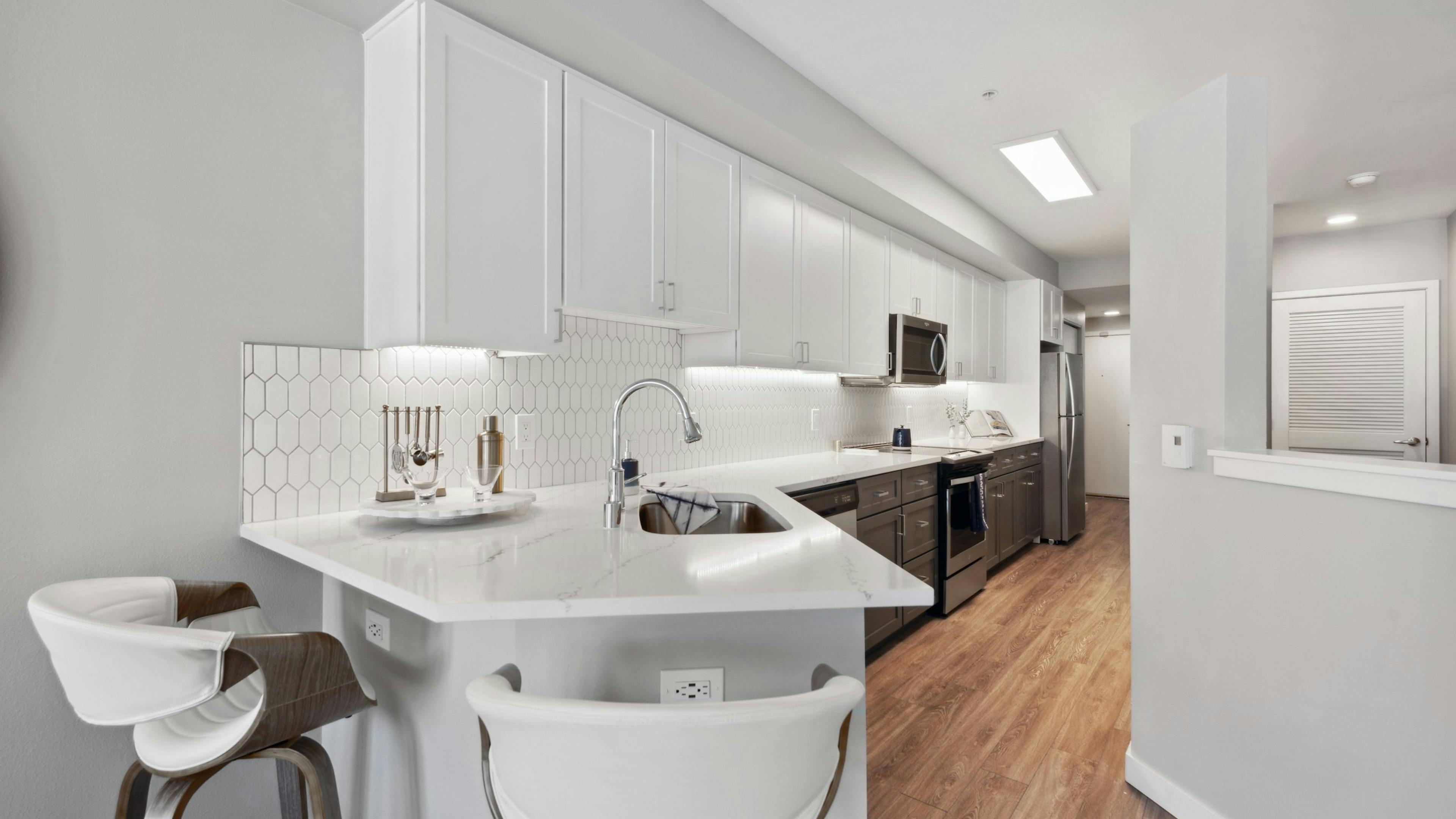 Kitchen with white cabinets and white countertop with stainless steel appliances and wood flooring at AMLI 535 apartments