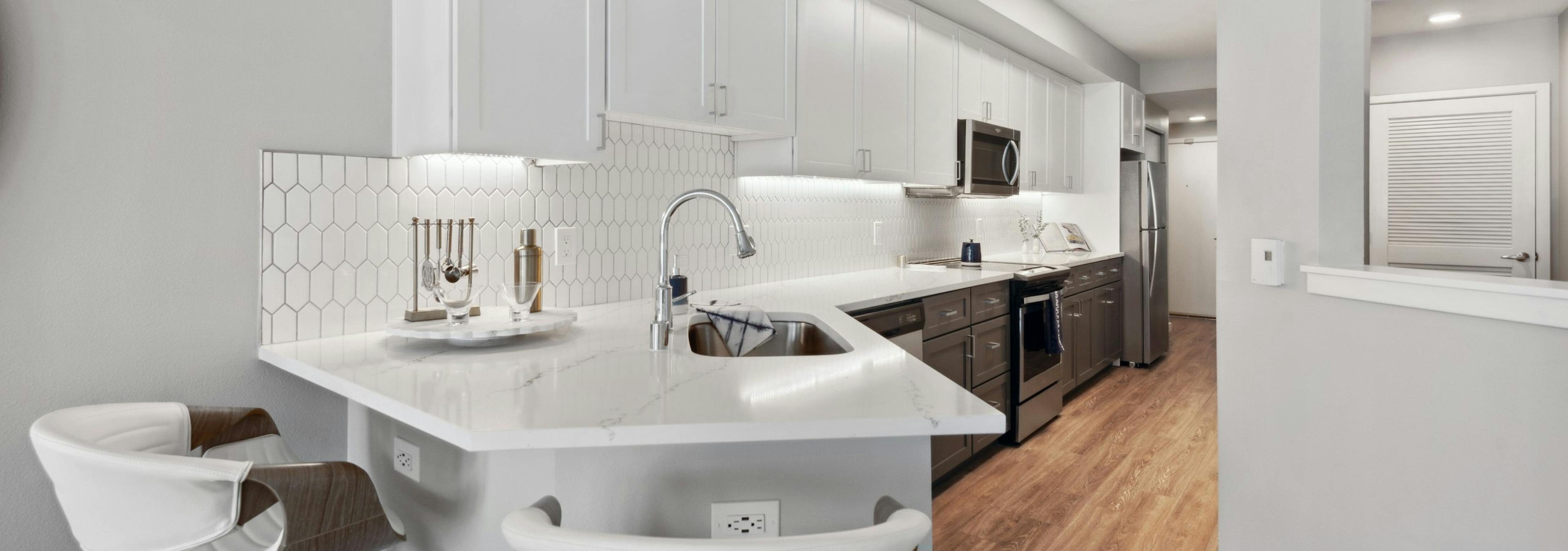 Kitchen with white cabinets and white countertop with stainless steel appliances and wood flooring at AMLI 535 apartments