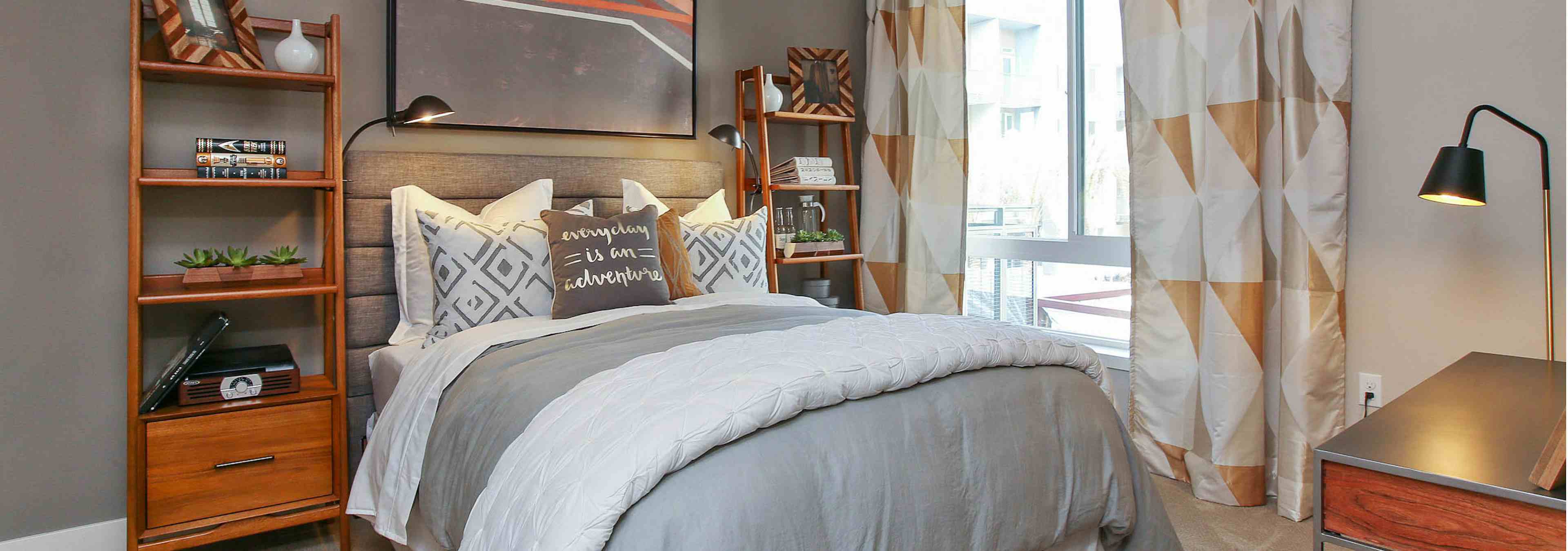 Interior view of AMLI Uptown Orange apartment bedroom with full bed, night stands and large window overlooking pool courtyard