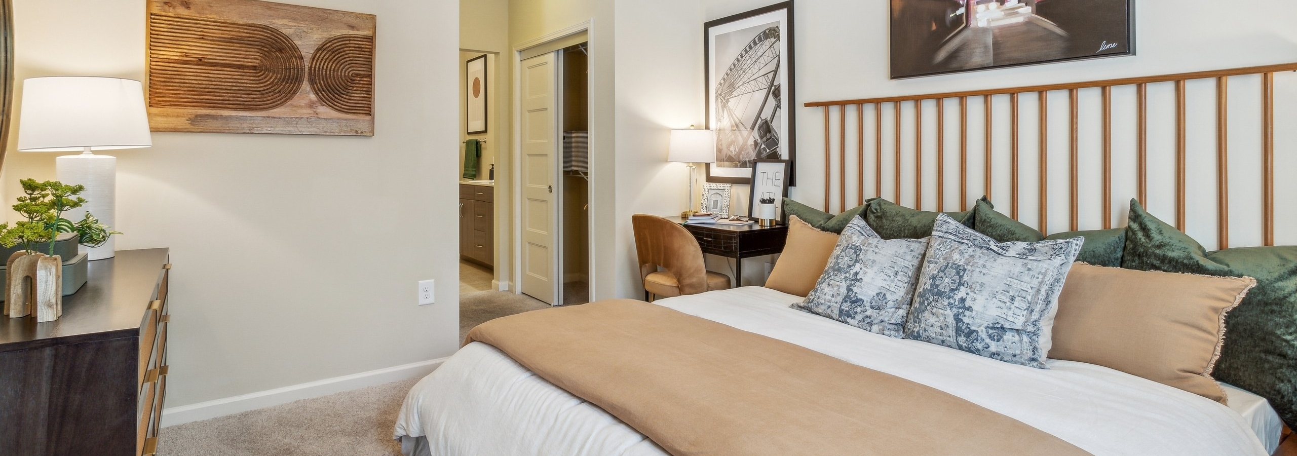 AMLI Ponce Park apartment bedroom with large bed with headboard and cream walls with artwork and view into hall to bathroom