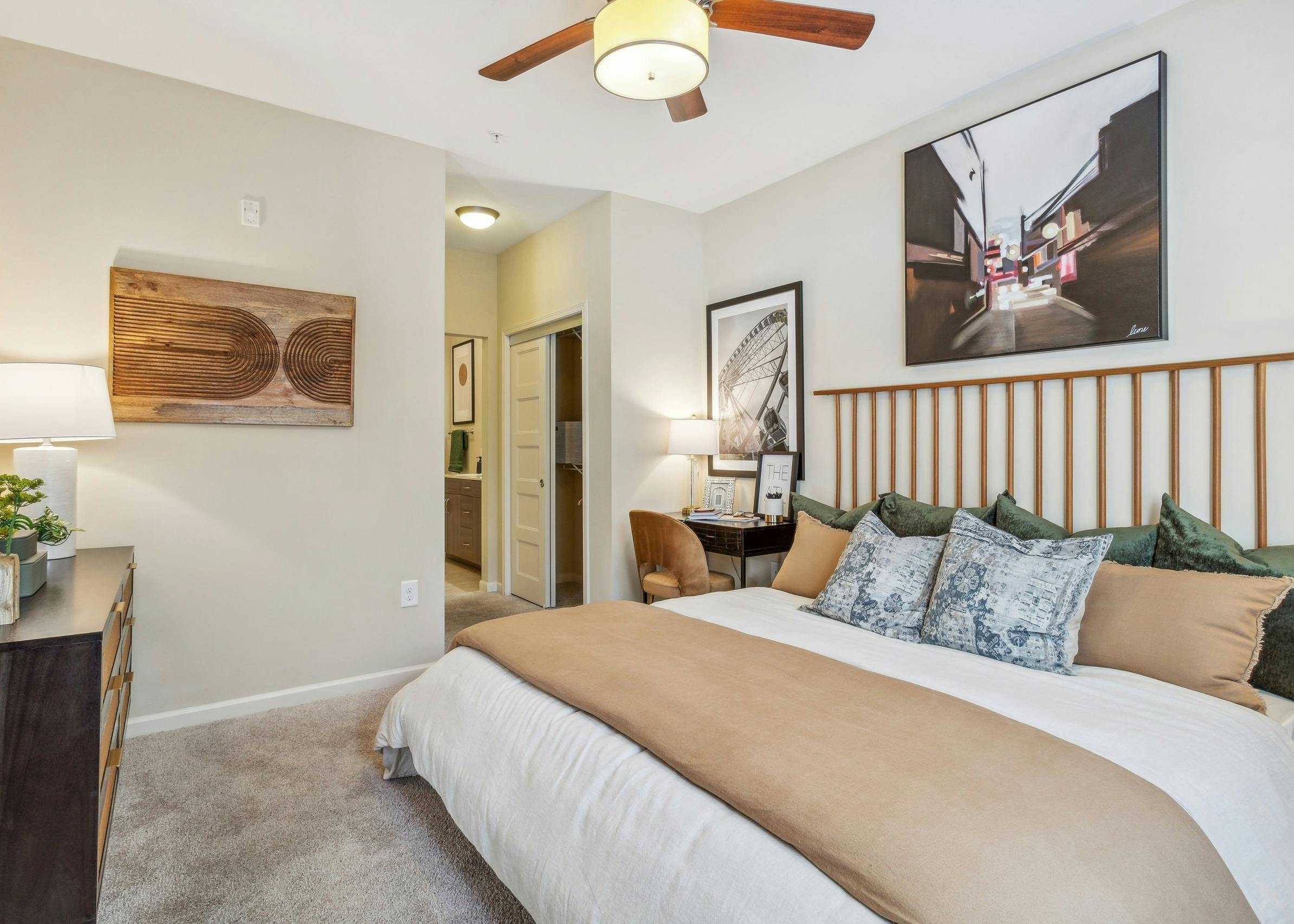 AMLI Ponce Park apartment bedroom with large bed with headboard and cream walls with artwork and view into hall to bathroom