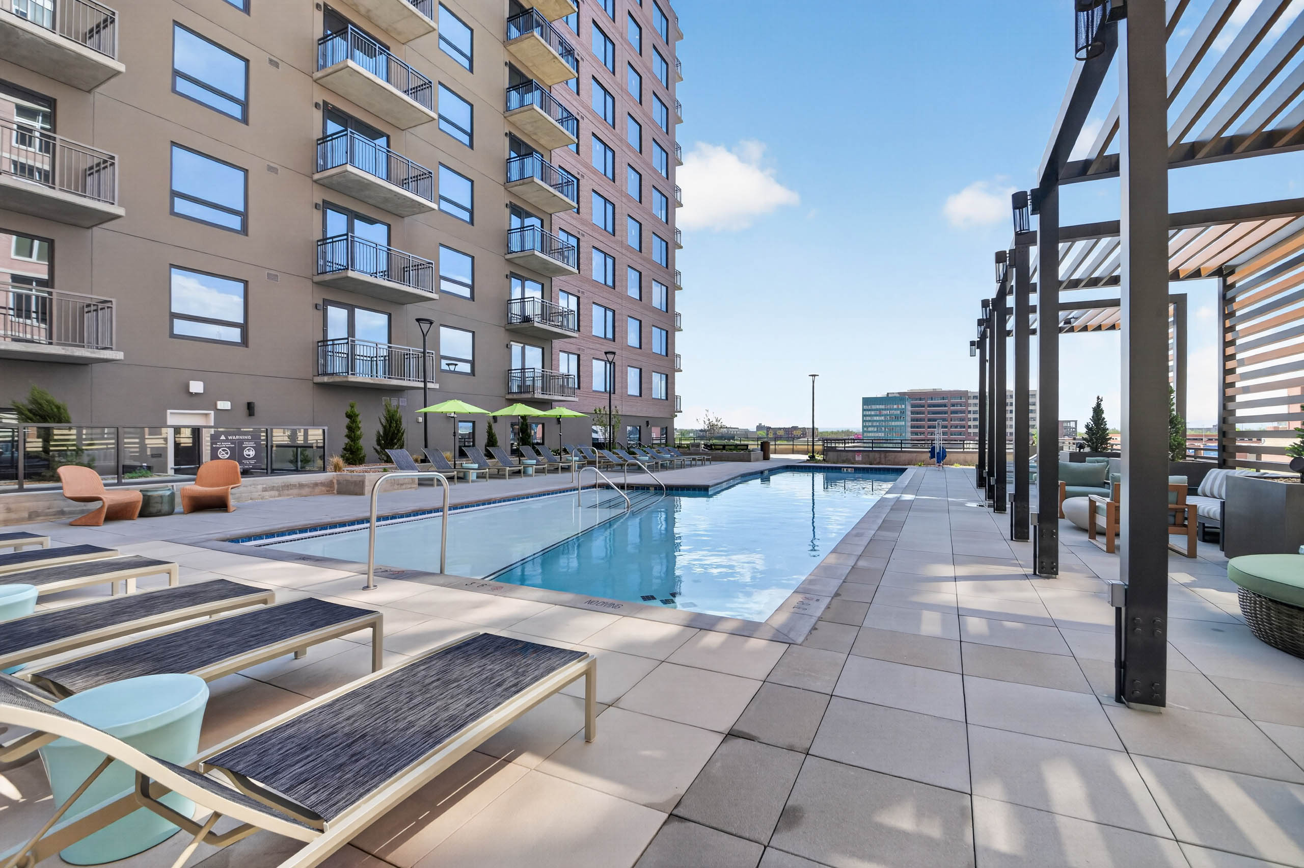 Daytime view of residential pool at AMLI Golden Triangle apartments surrounded by lounge chairs and cabanas and umbrellas