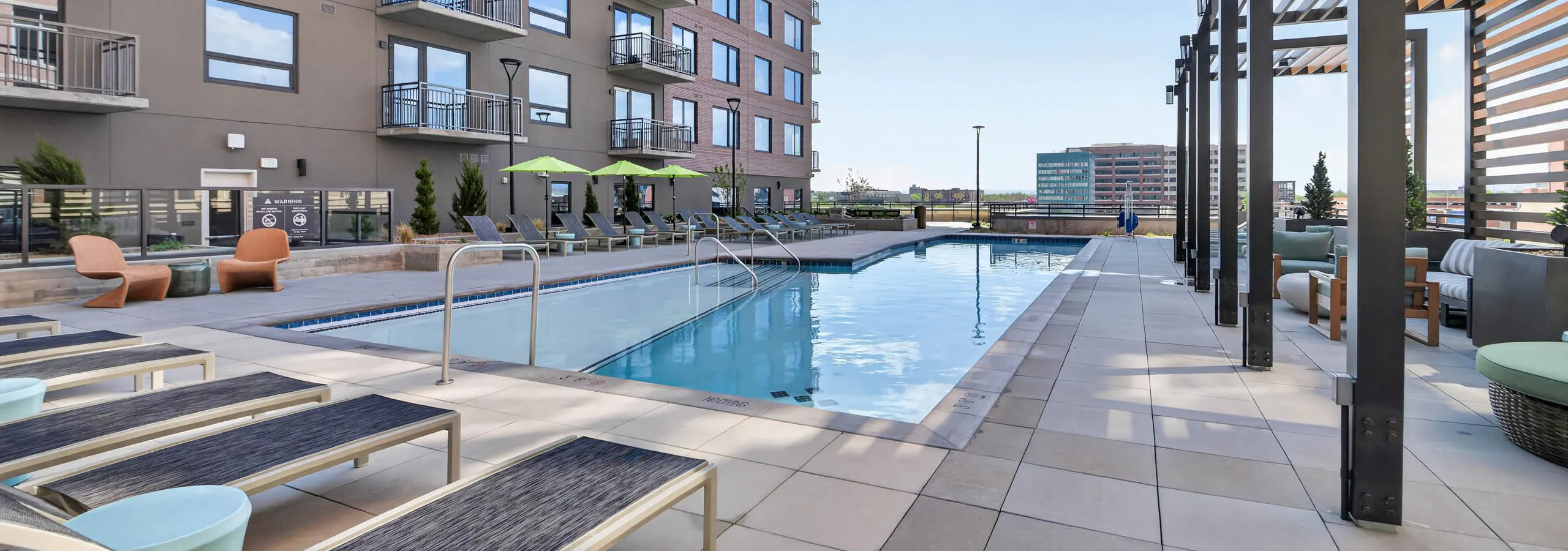 Daytime view of residential pool at AMLI Golden Triangle apartments surrounded by lounge chairs and cabanas and umbrellas