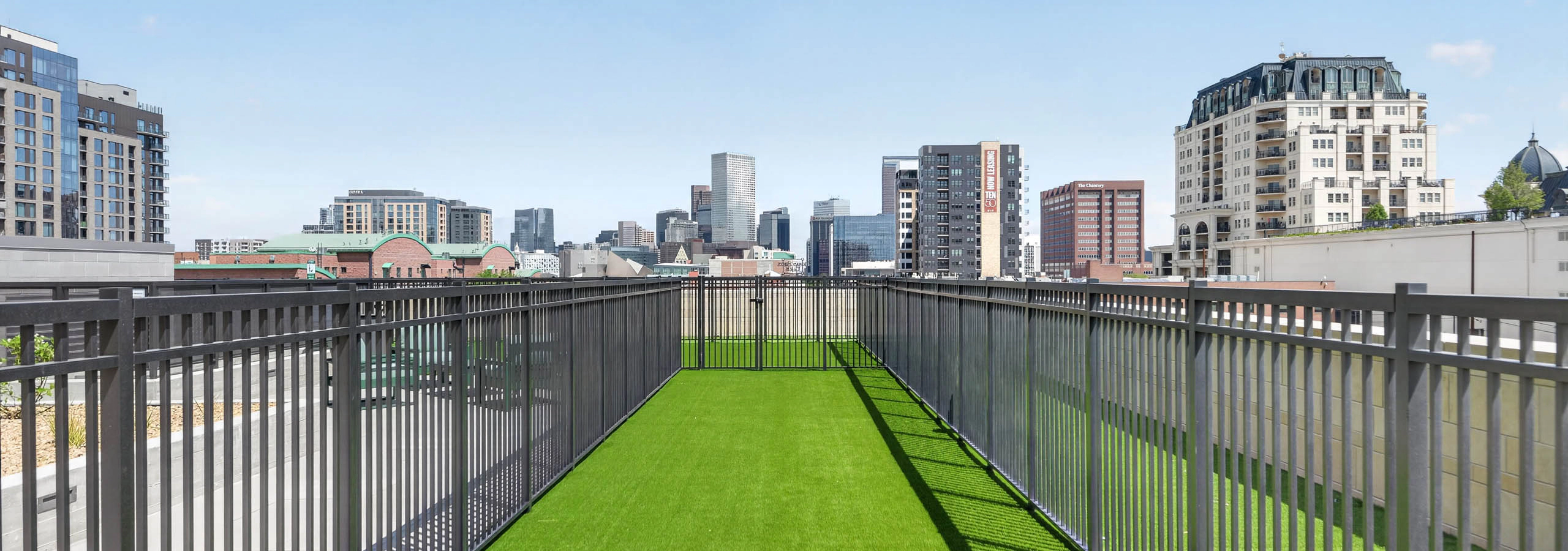 Resident dog run at AMLI Golden Triangle apartments with fenced turf area long walkway and downtown skyline views