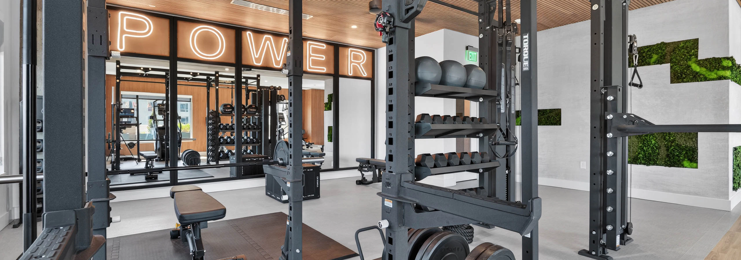 Modern gym at AMLI Golden Triangle apartments with power racks free weights training zone and illuminated signage
