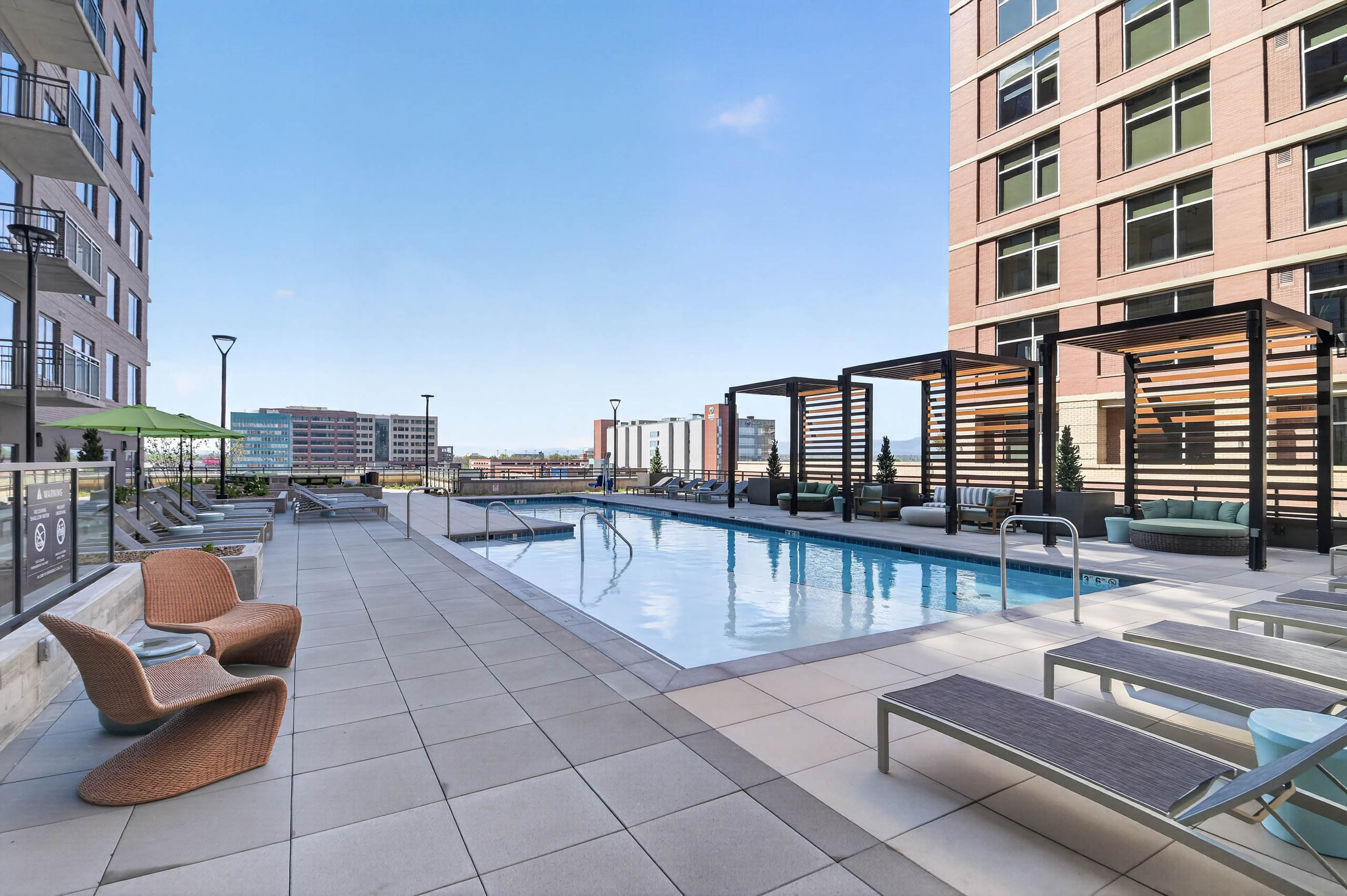 Resident pool at AMLI Golden Triangle apartments with lap pool lounge chairs pergola seating and city skyline views
