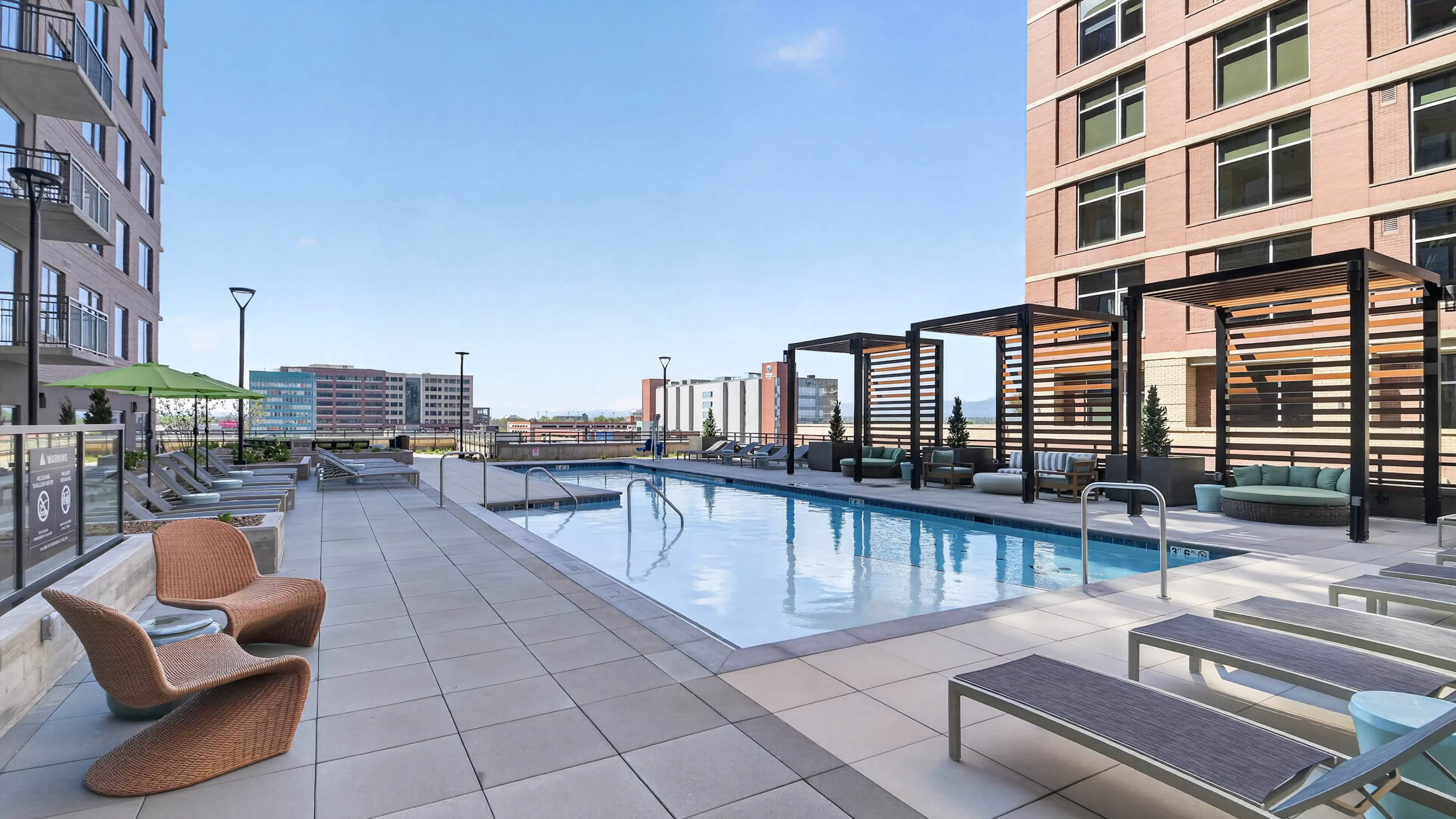 Resident pool at AMLI Golden Triangle apartments with lap pool lounge chairs pergola seating and city skyline views