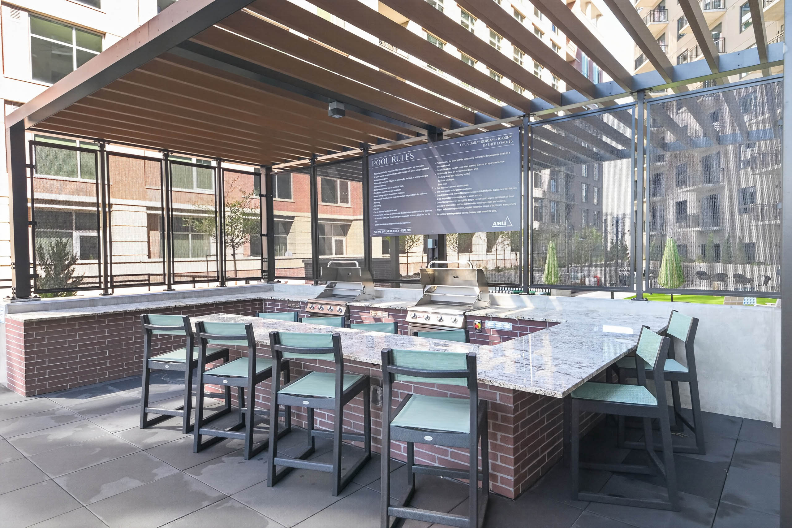 Outdoor grilling area at AMLI Golden Triangle apartments with stainless grills bar seating pergola and city views
