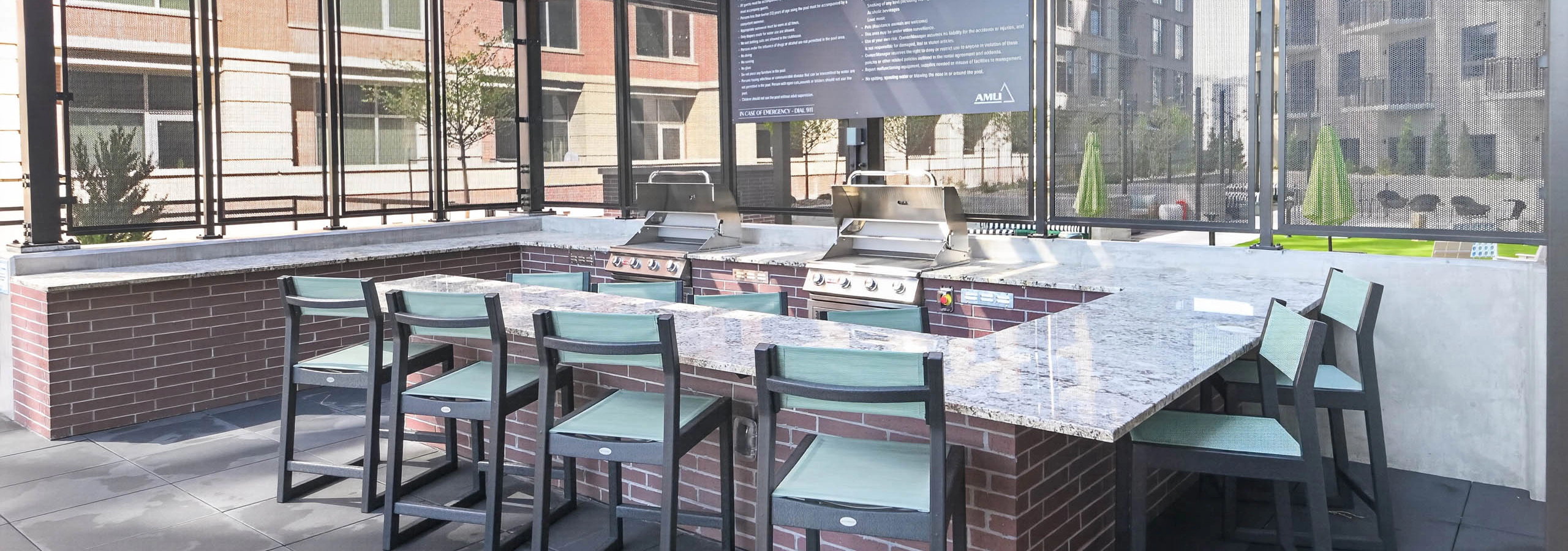 Outdoor grilling area at AMLI Golden Triangle apartments with stainless grills bar seating pergola and city views