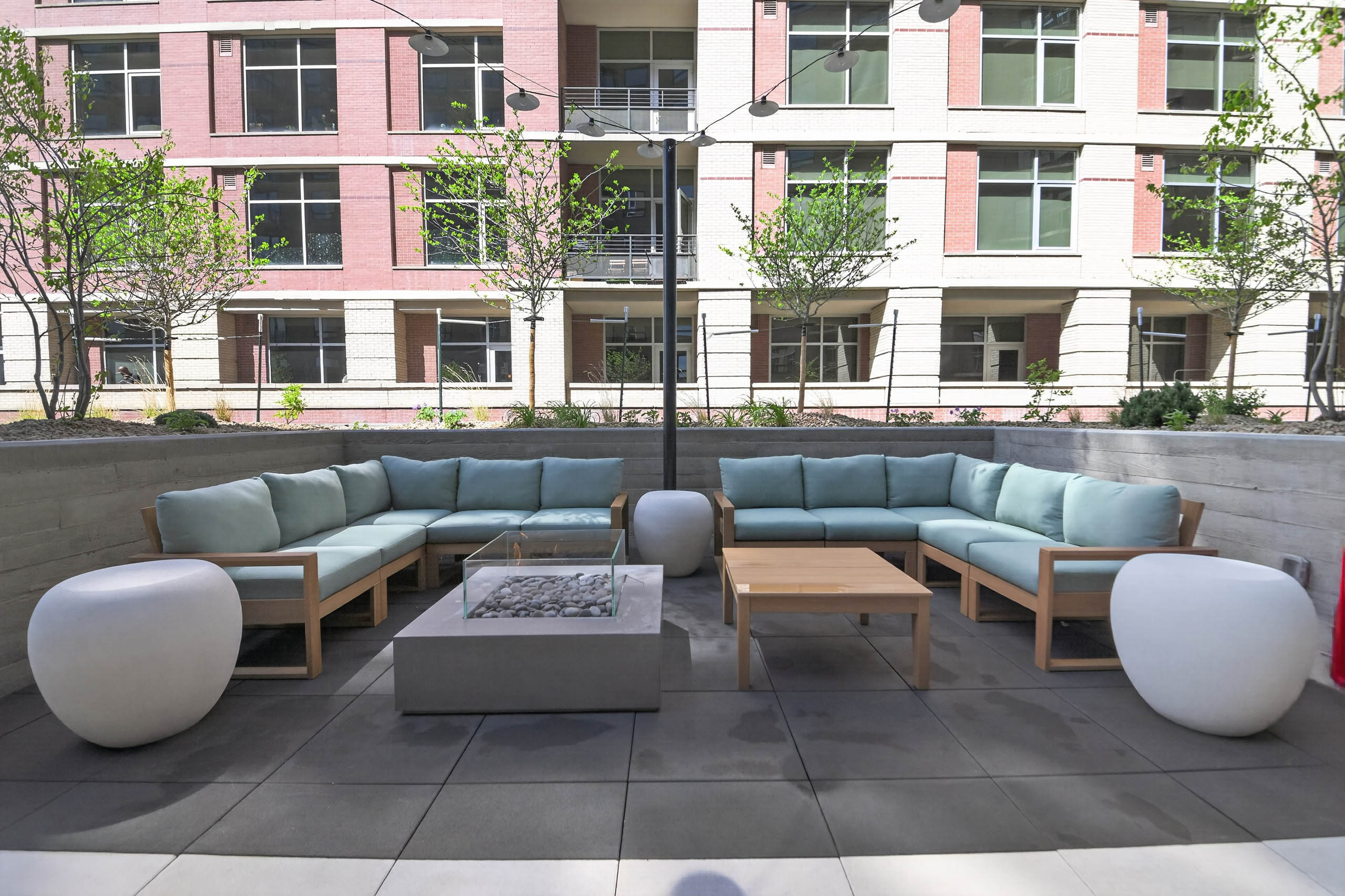 Outdoor lounge at AMLI Golden Triangle apartments with sectional seating fire pit string lights and landscaped courtyard