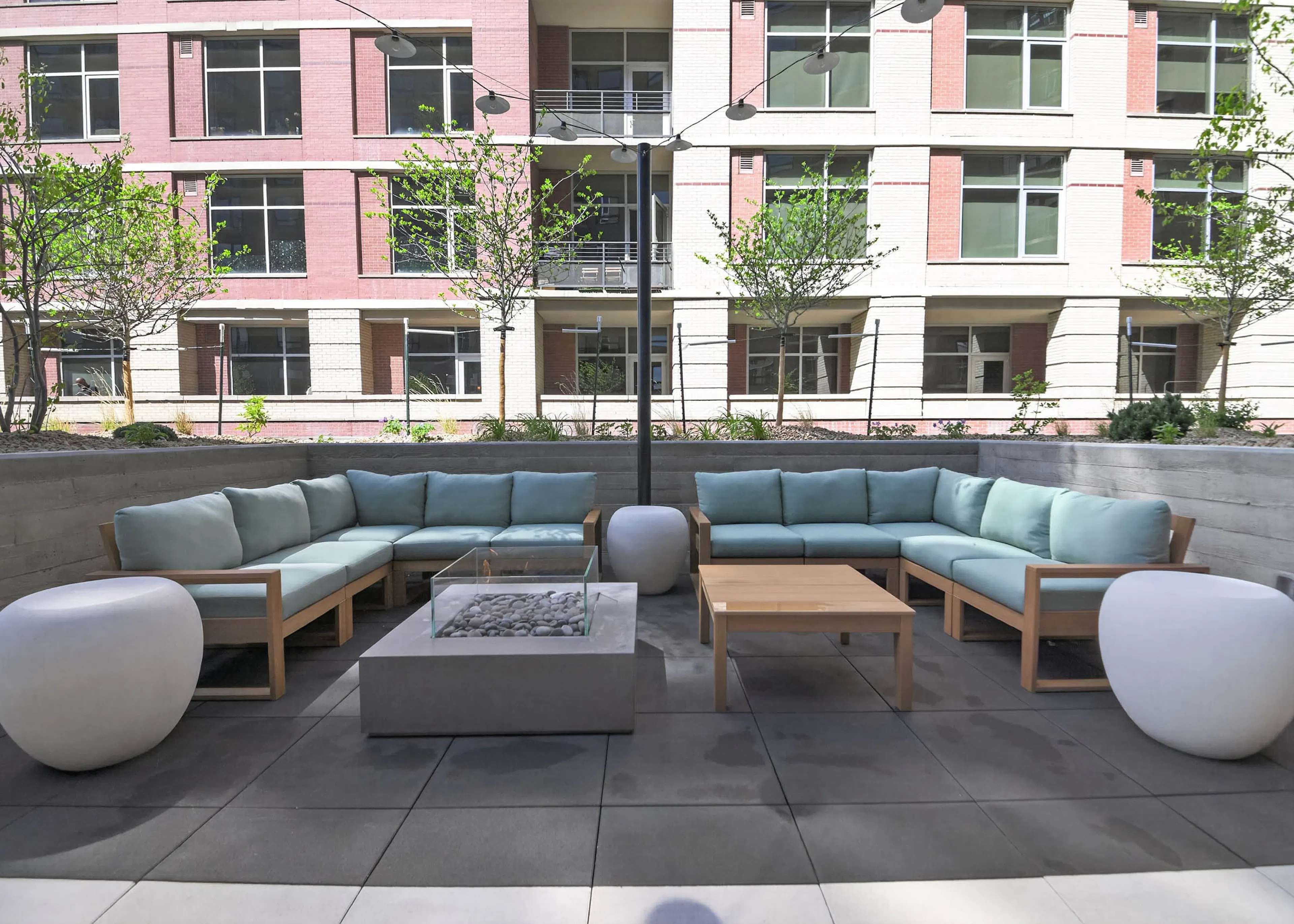 Outdoor lounge at AMLI Golden Triangle apartments with sectional seating fire pit string lights and landscaped courtyard