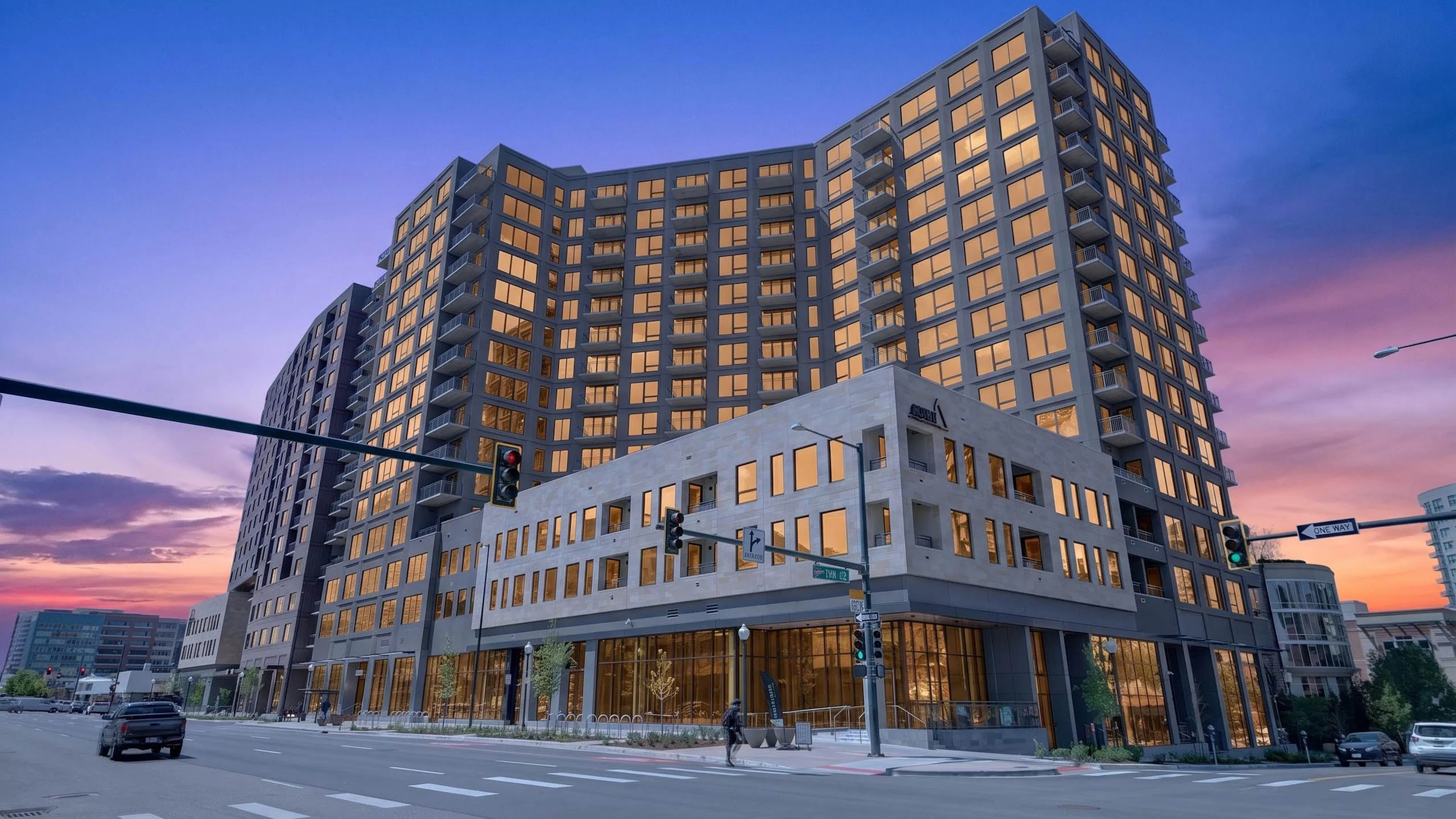 Twilight exterior of AMLI Golden Triangle apartment building with illuminated windows corner intersection and evening sky