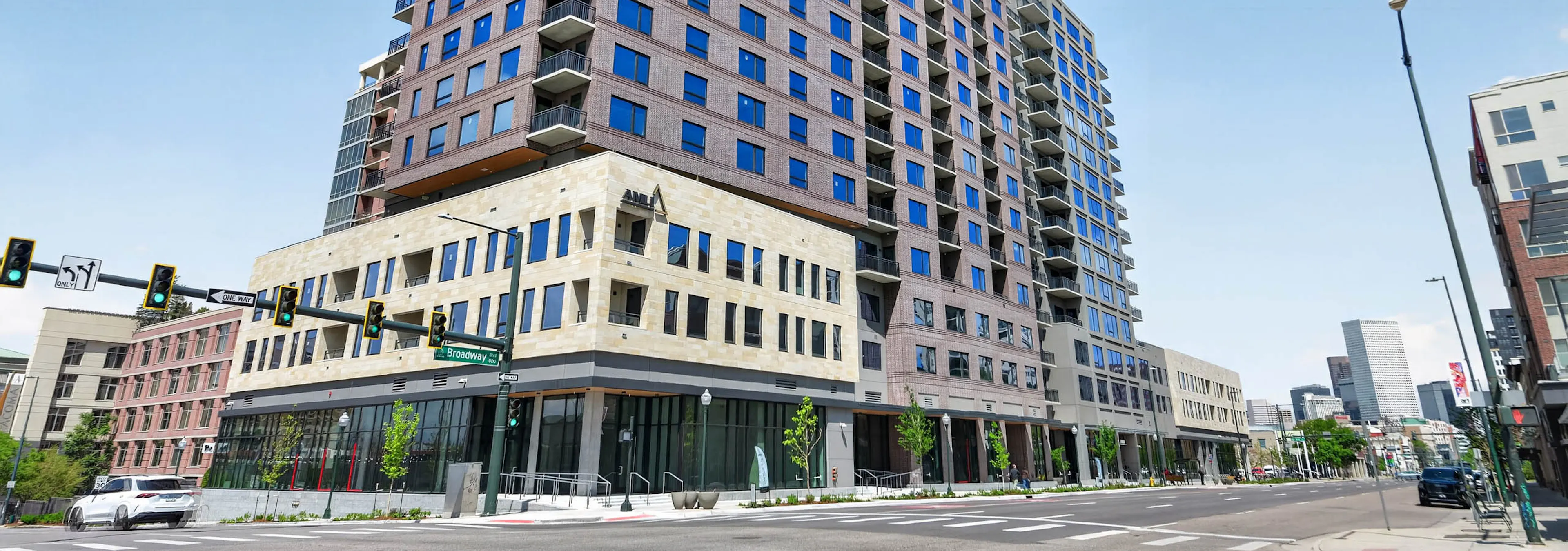 Wide street view of AMLI Golden Triangle apartment building with brick facade ground level storefronts and city intersection