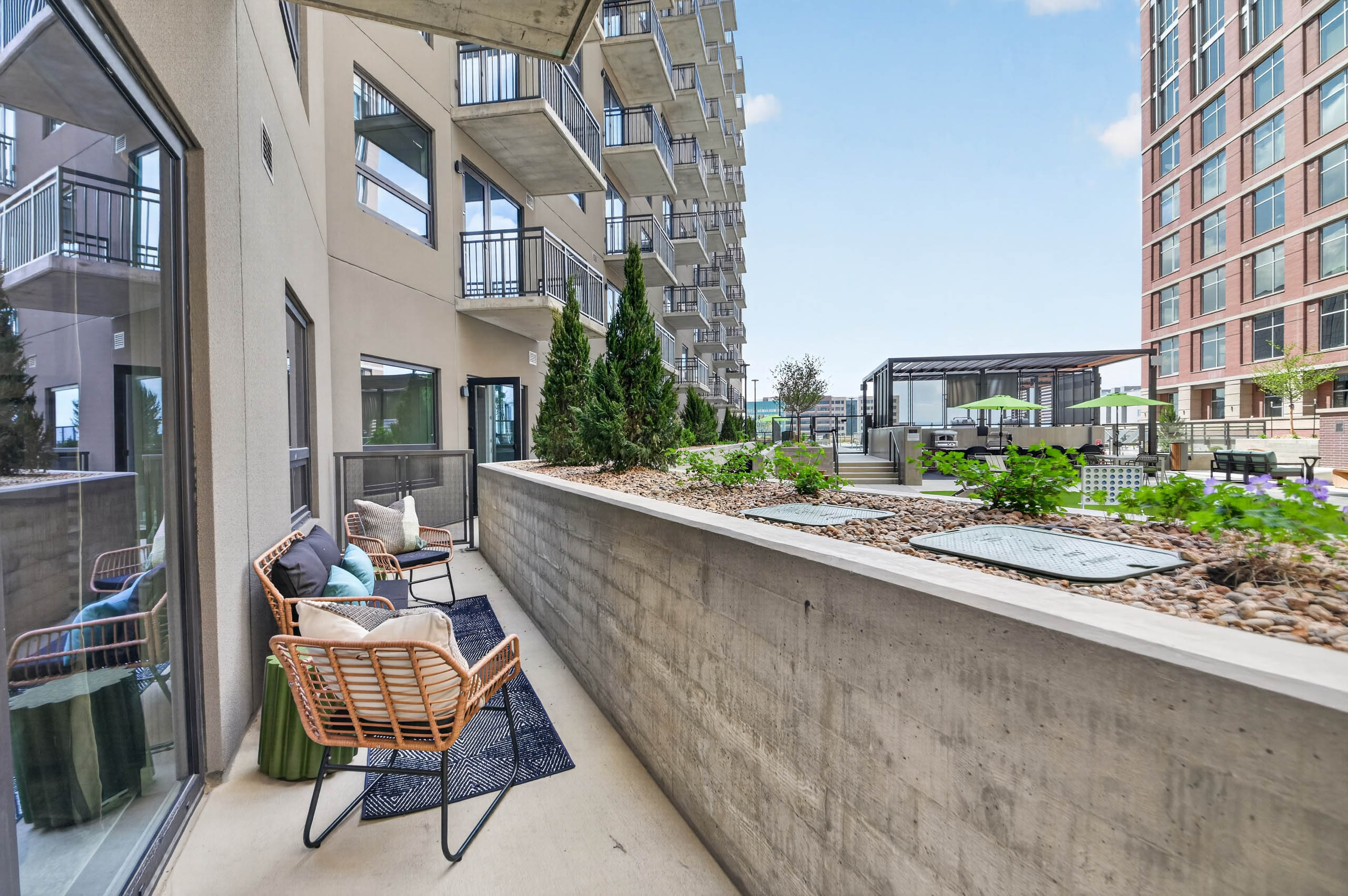 Private patio at AMLI Golden Triangle apartment with woven chairs balcony railing landscaped courtyard and nearby seating
