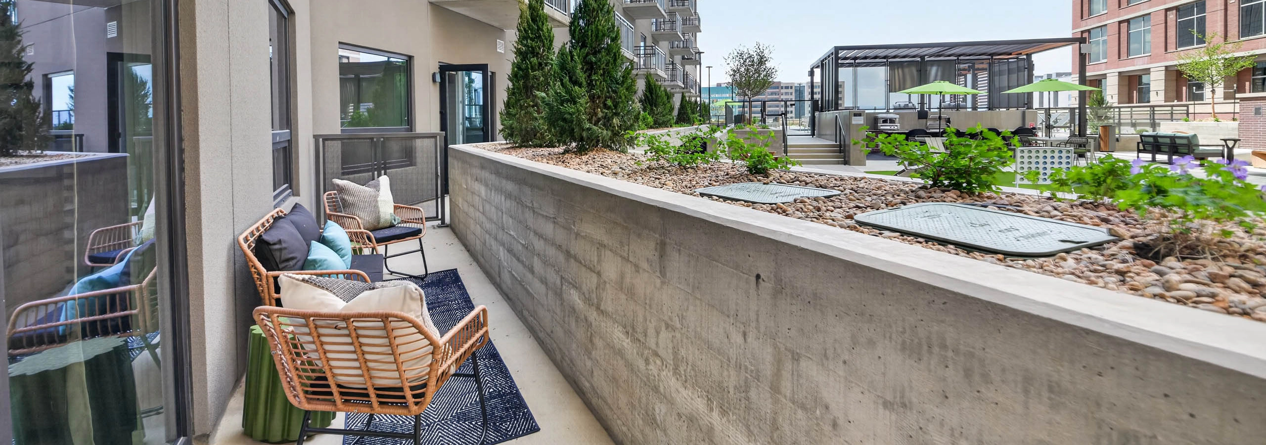 Private patio at AMLI Golden Triangle apartment with woven chairs balcony railing landscaped courtyard and nearby seating
