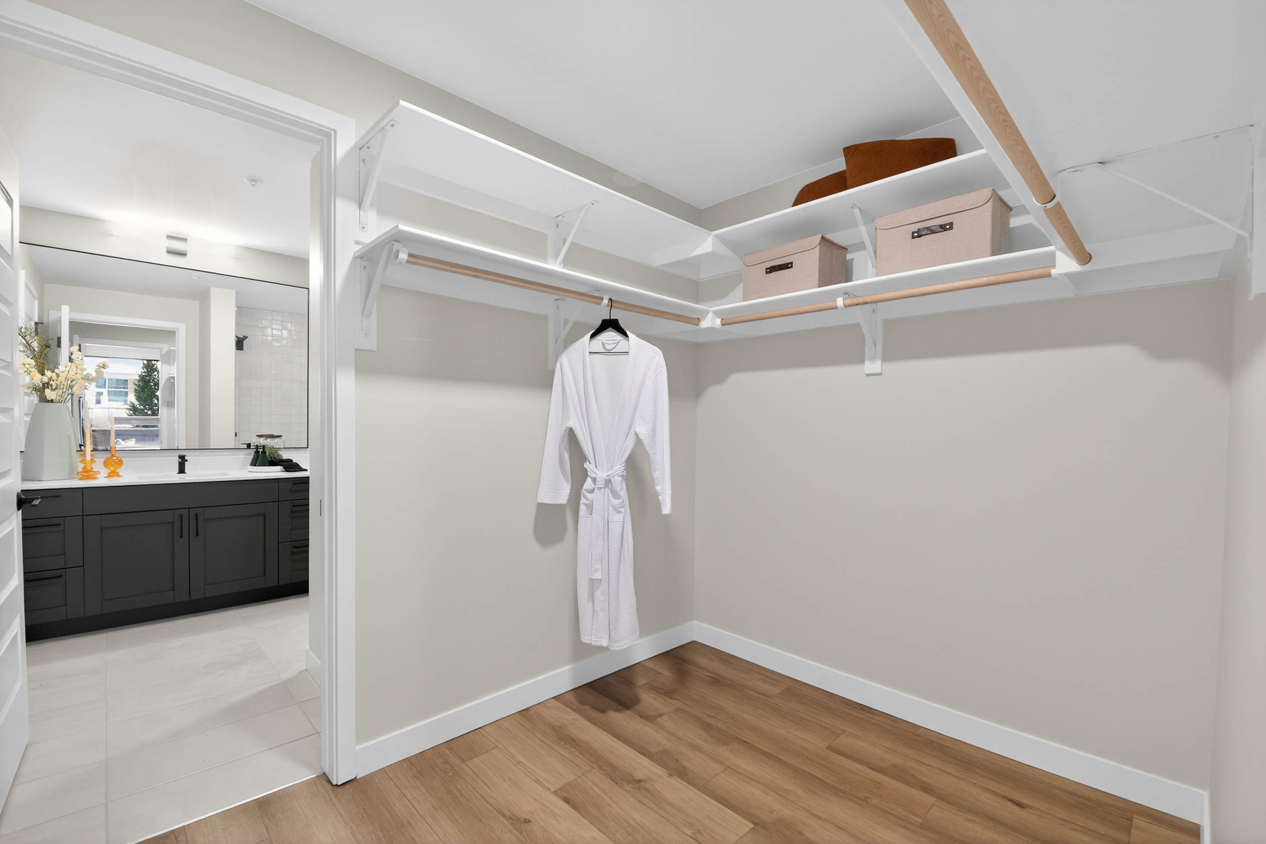 Walk in closet at AMLI Golden Triangle apartment with built in shelving hanging rods storage bins and wood flooring