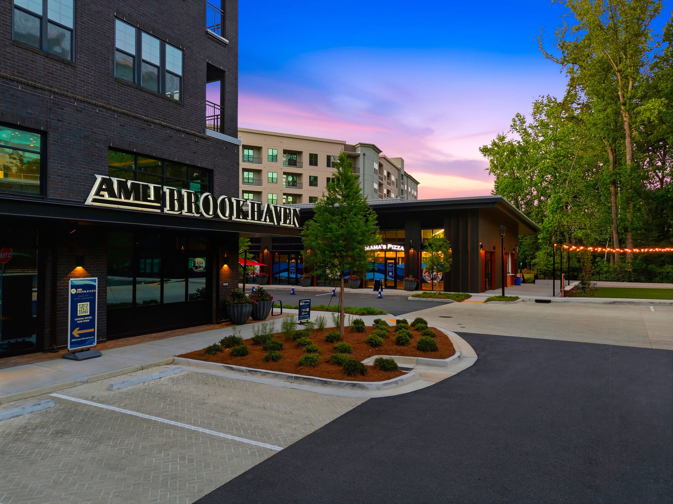 Retail exterior at AMLI Brookhaven with modern design, evening lighting, and office buildings in the background.