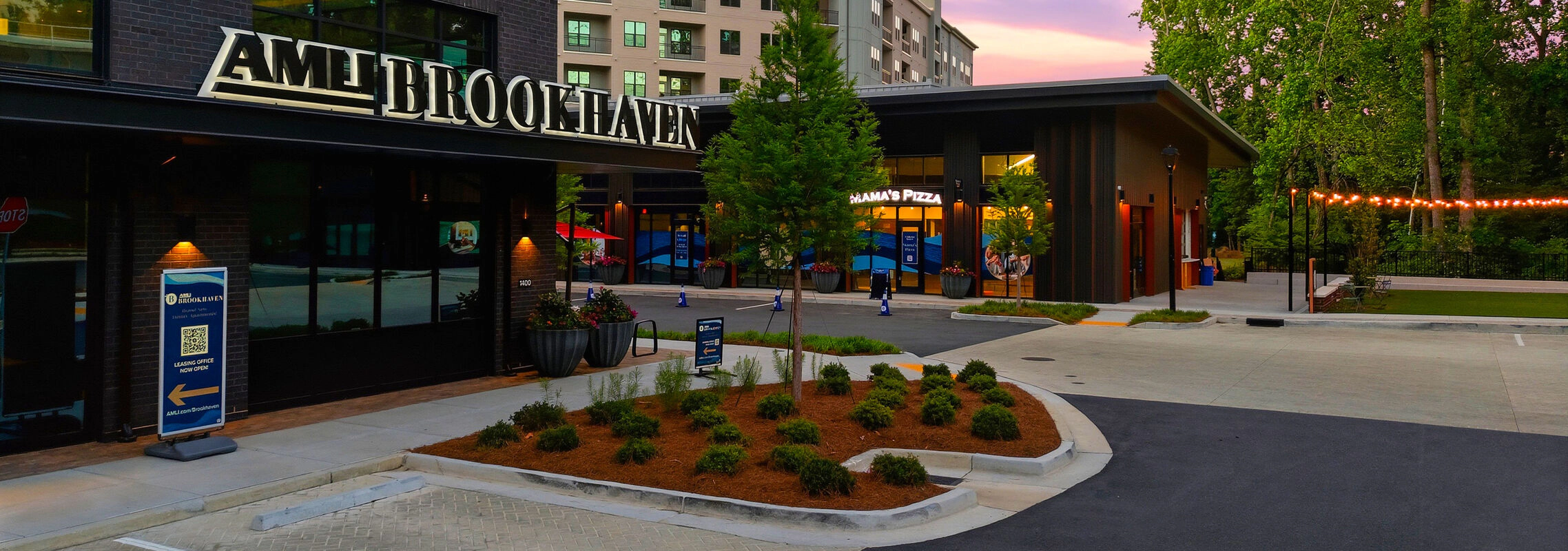 Retail exterior at AMLI Brookhaven with modern design, evening lighting, and office buildings in the background.
