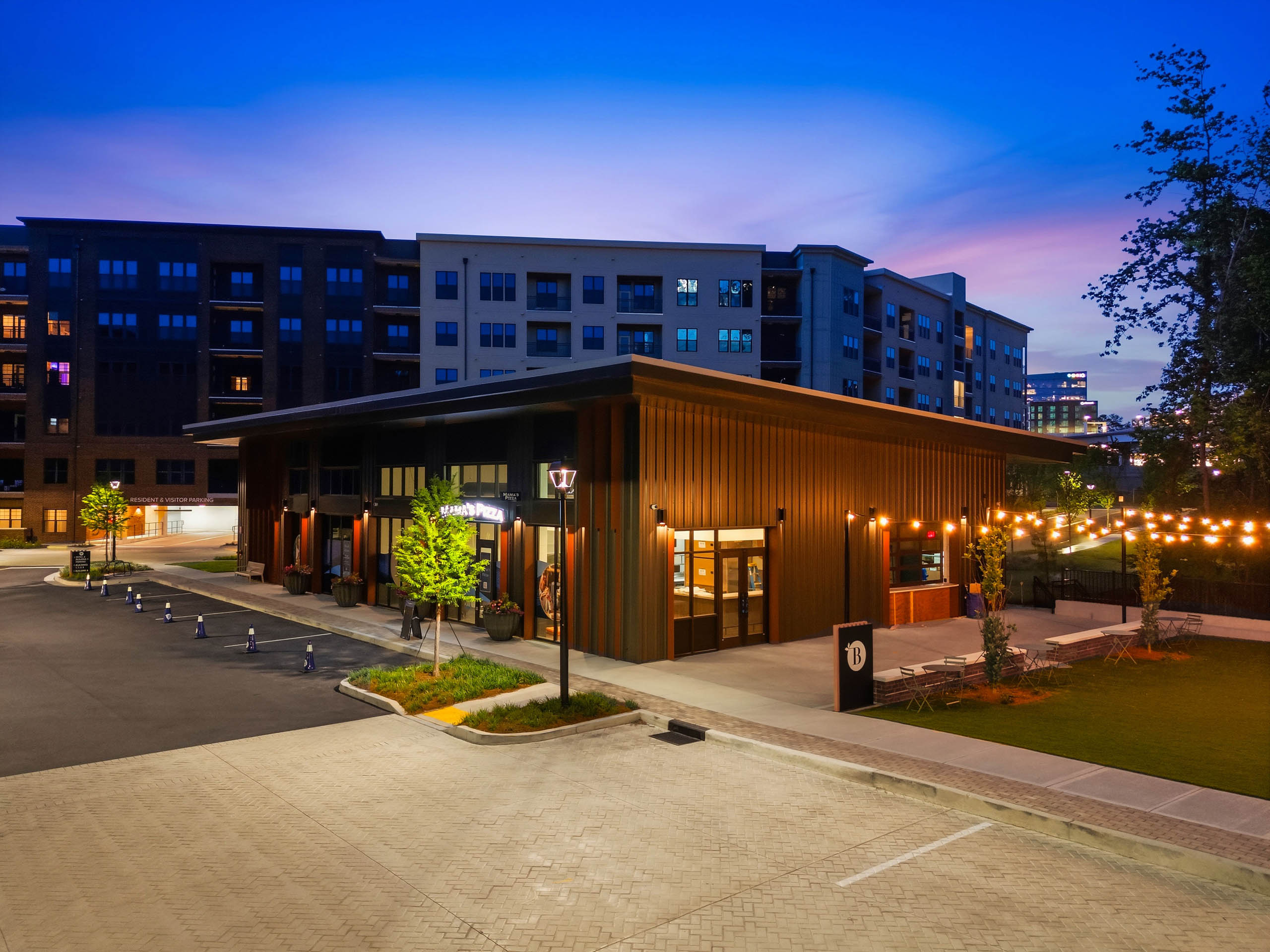 Exterior view of AMLI Brookhaven onsite retail featuring Mama’s Pizza with outdoor lawn seating and string lighting.