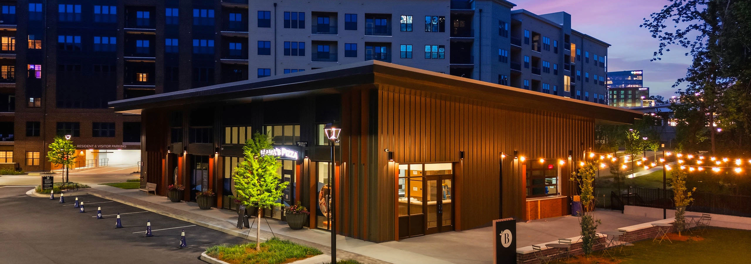 Exterior view of AMLI Brookhaven onsite retail featuring Mama’s Pizza with outdoor lawn seating and string lighting.