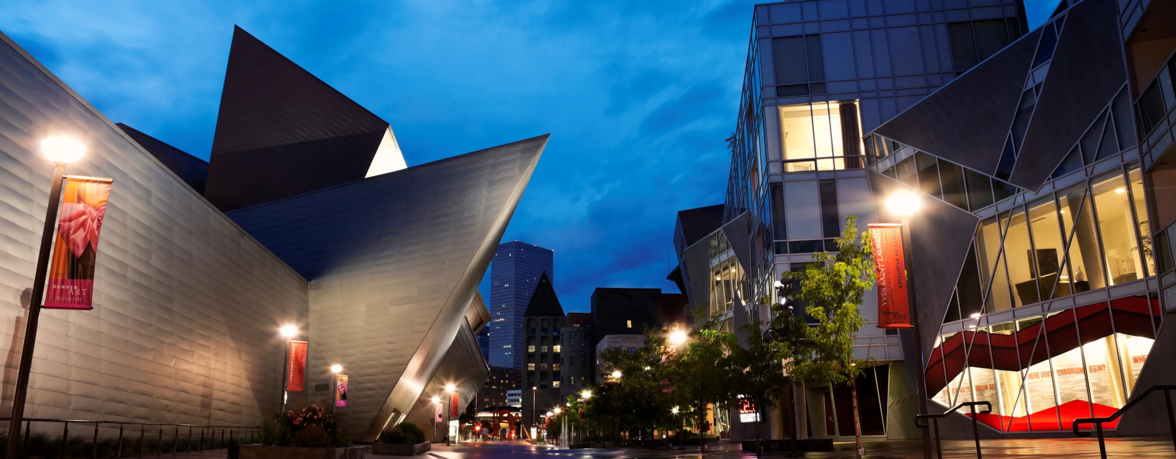 An evening street view of the Denver Art Museum's striking, angular modern architecture under a deep blue twilight sky.