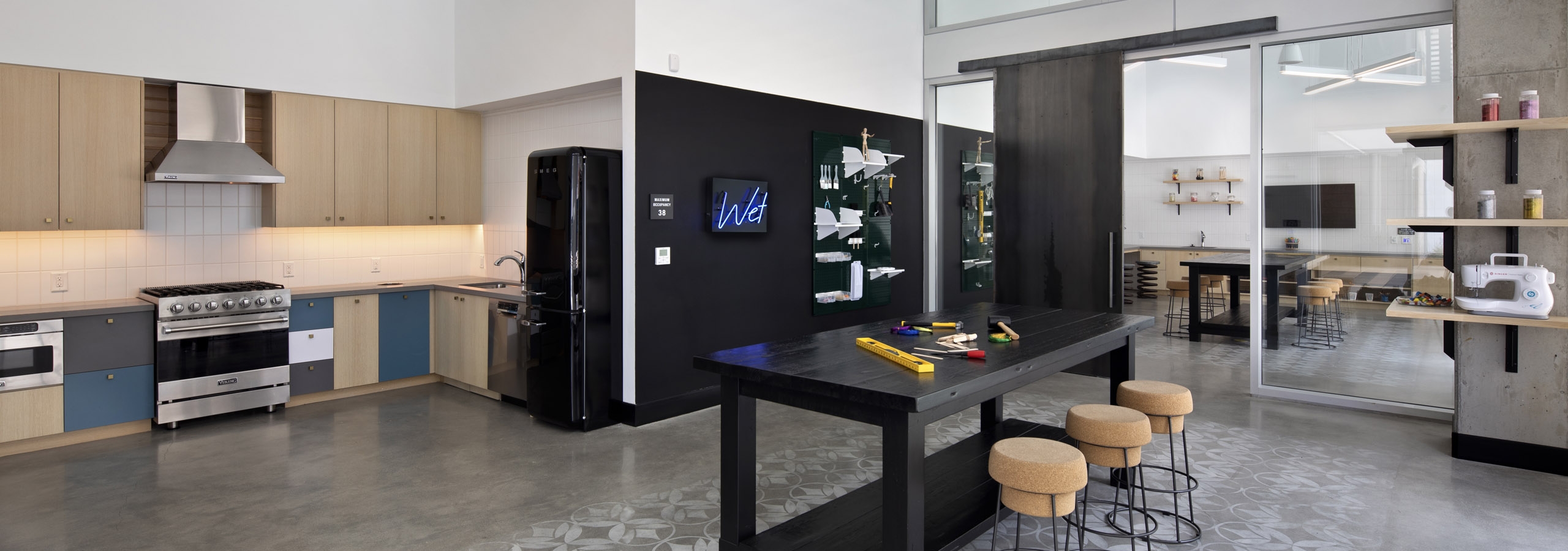 Arts and crafts maker space with catering kitchen and black table with three cork stools at AMLI Park Broadway apartments