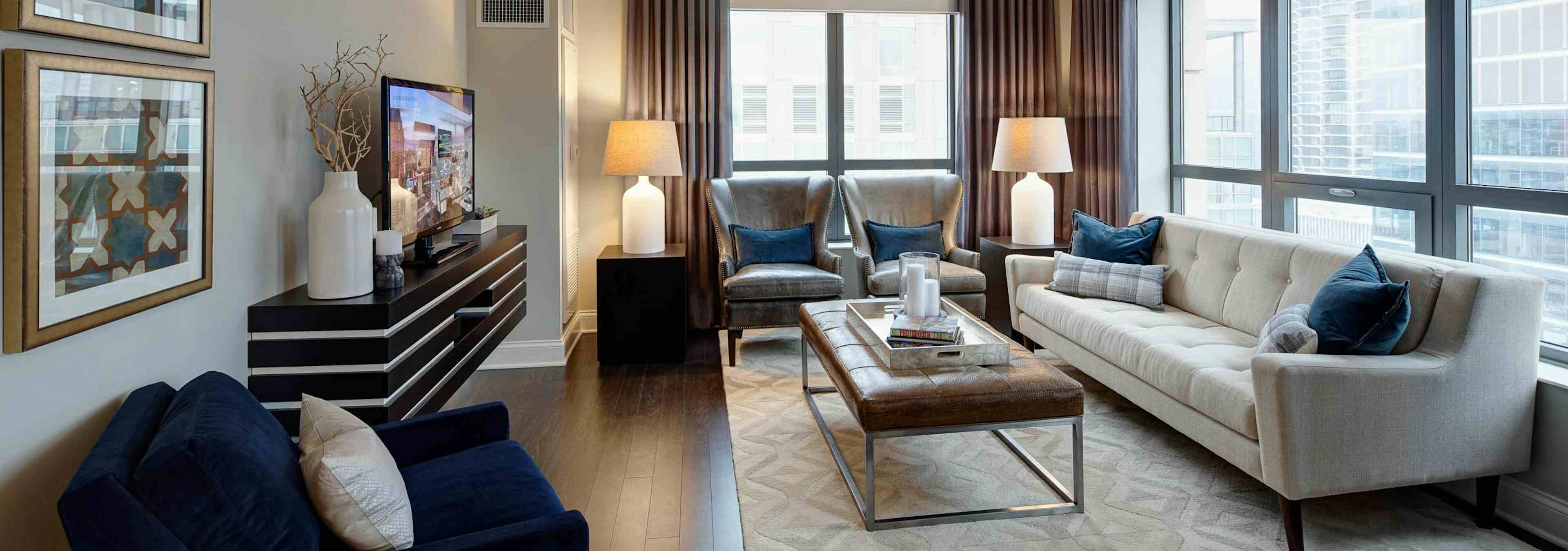 AMLI River North living room with ceiling to floor windows and a white leather sofa with brown and dark turquoise decor