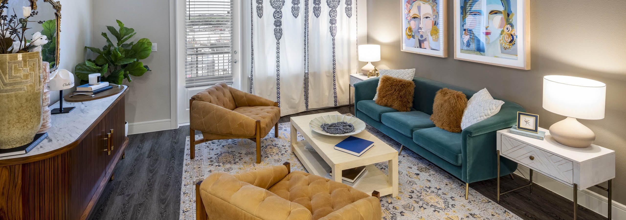 View of AMLI Lakeline apartment living room with dark orange leather chairs and a blue plush sofa on top of a colorful rug