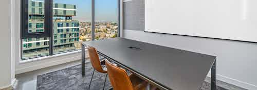 Conference room at AMLI Arc apartment building with table and two brown chairs facing a white board and wall of windows
