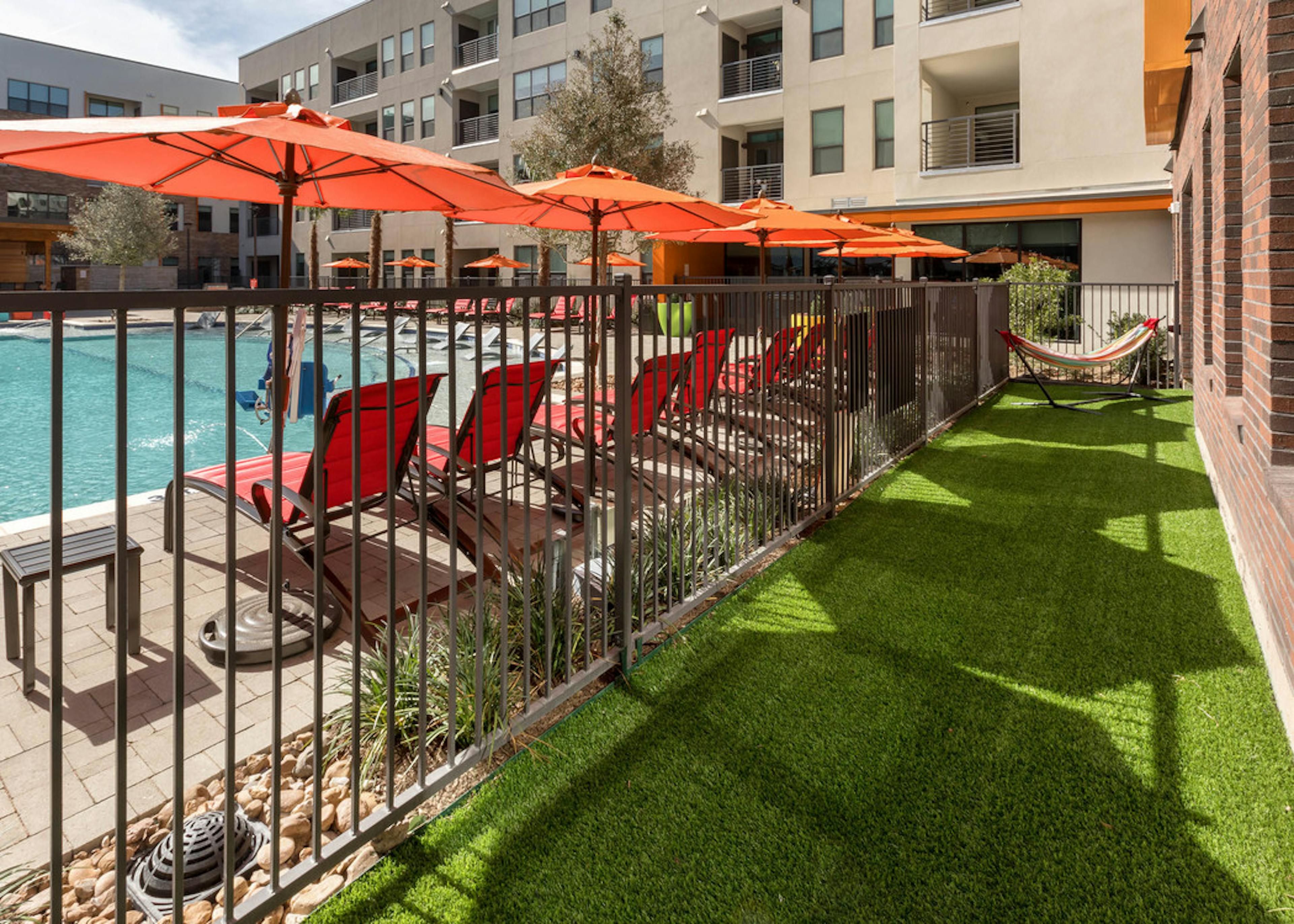 Close up view through resident fenced yard of lounge chairs under orange umbrellas in swimming pool area