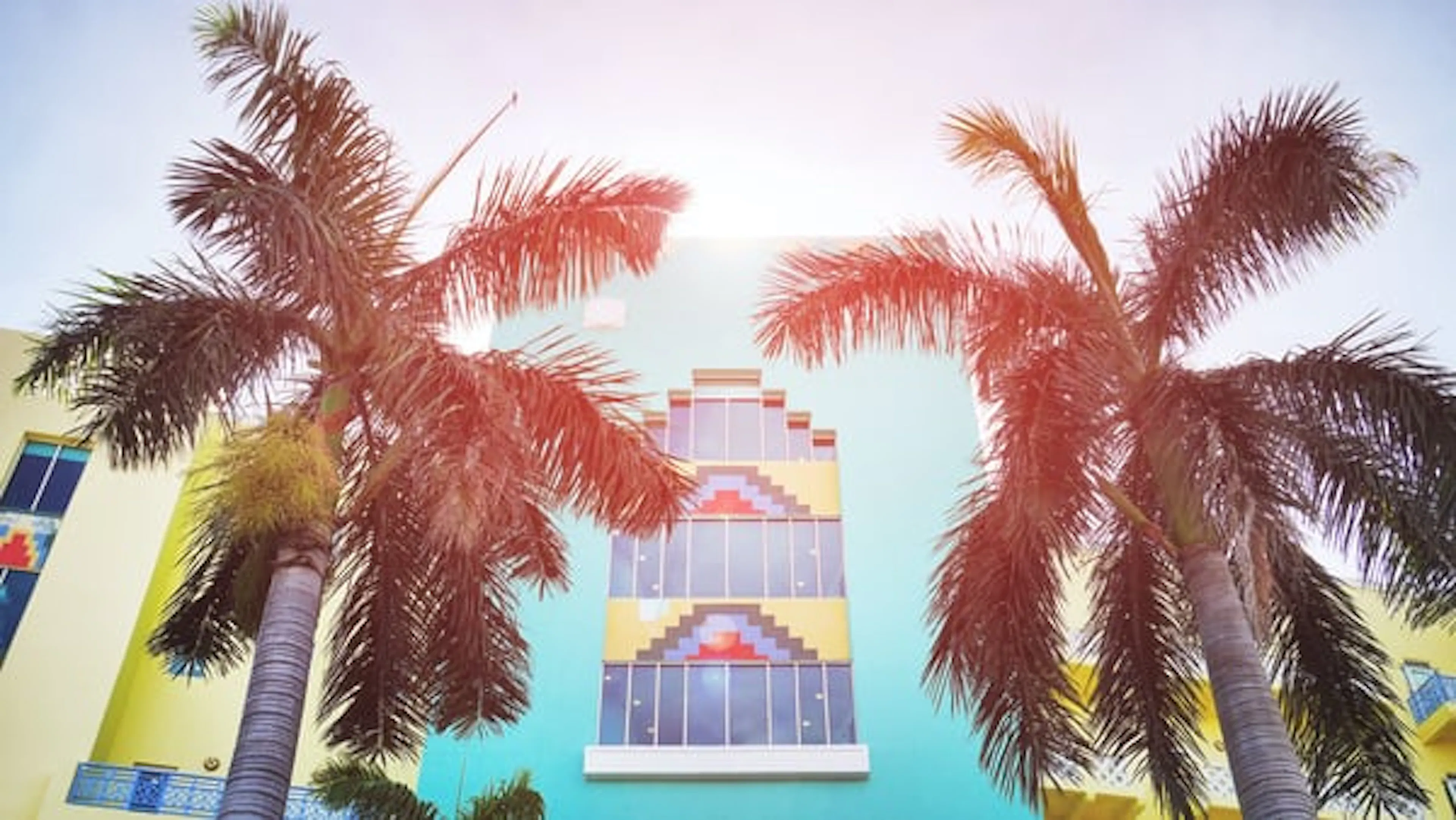 Two palm trees in front of a sunny blue house with stepped windows and blocks of contrasting color in art deco style