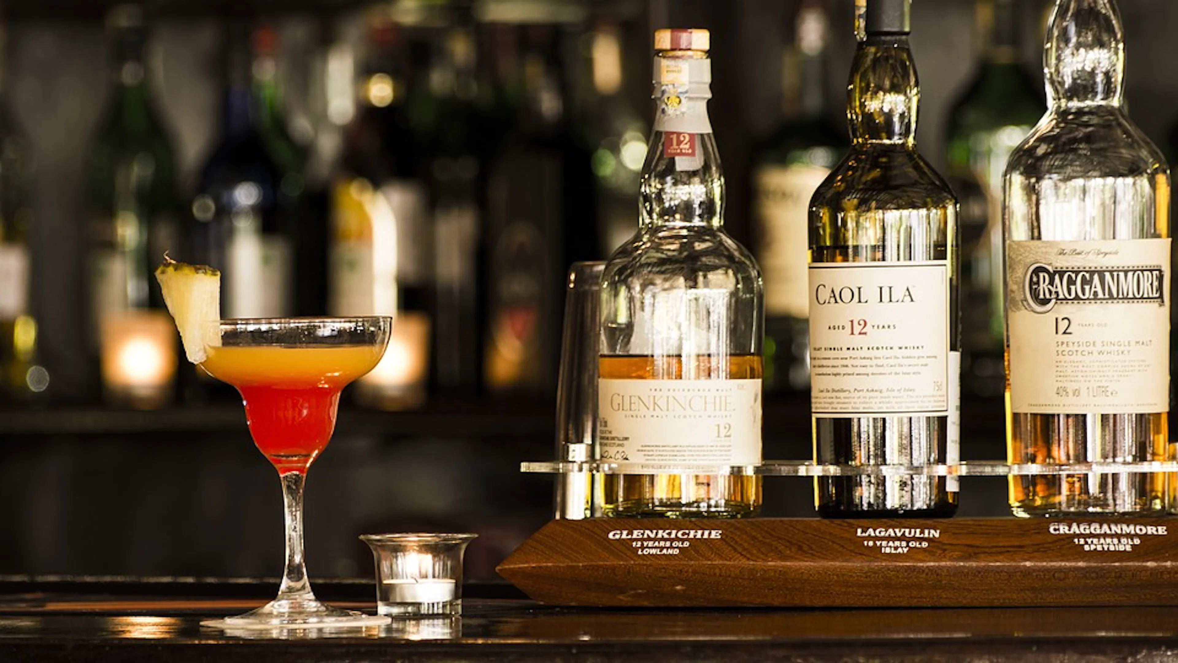 A glass of colorful drink in a margarita glass next to three glass bottles of liquor